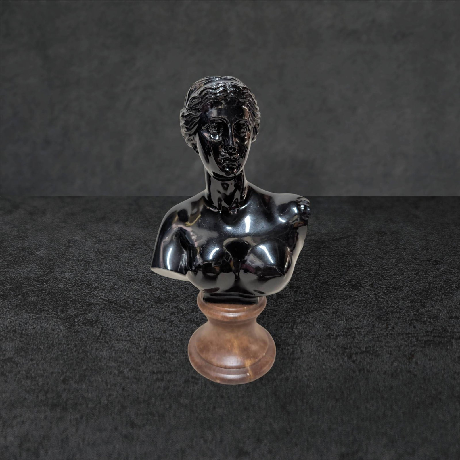 Black Amethyst Glass Venus Bust on Wooden Base: Black amethyst glass bust of Venus mounted on a turned wooden base. The sculpture measures 9 1/2 inches tall, 5 inches wide, and 3 inches deep. The bust displays smooth, detailed craftsmanship with a 
