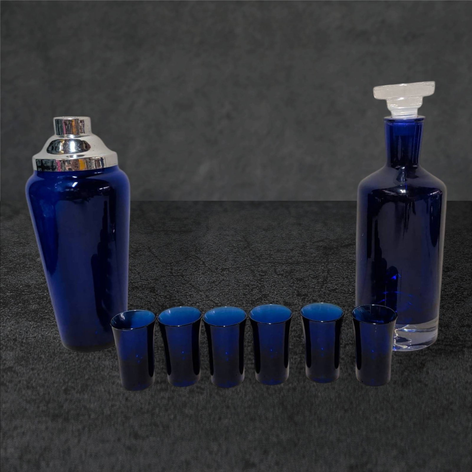 Cobalt Blue Decanter with Stopper, Shaker, and Six Shot Glasses: A cobalt blue decanter with stopper (11 1/2 in. tall), a cocktail shaker with chrome-tone lid (10 1/2 in. tall), and six matching cobalt blue shot glasses (each 2 3/4 in. tall). The glassware features