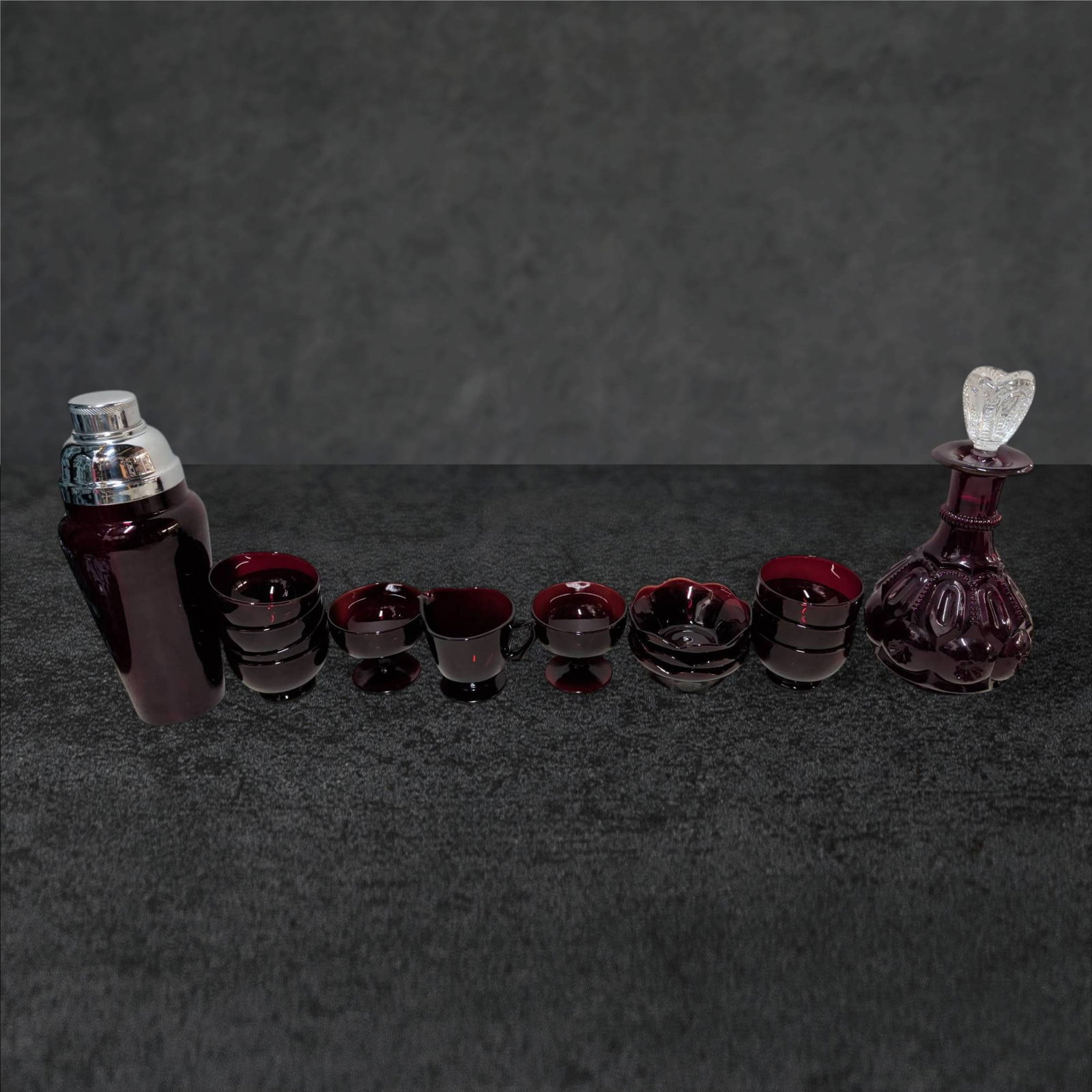 Ruby Red Glass Collection Including Decanter, Shaker, and Bowls: Ruby red glass collection comprising a decanter with a height of 11.5 inches, featuring an ornate stopper, and a matching shaker measuring 12 inches tall with a chrome lid. The set also includes bowls