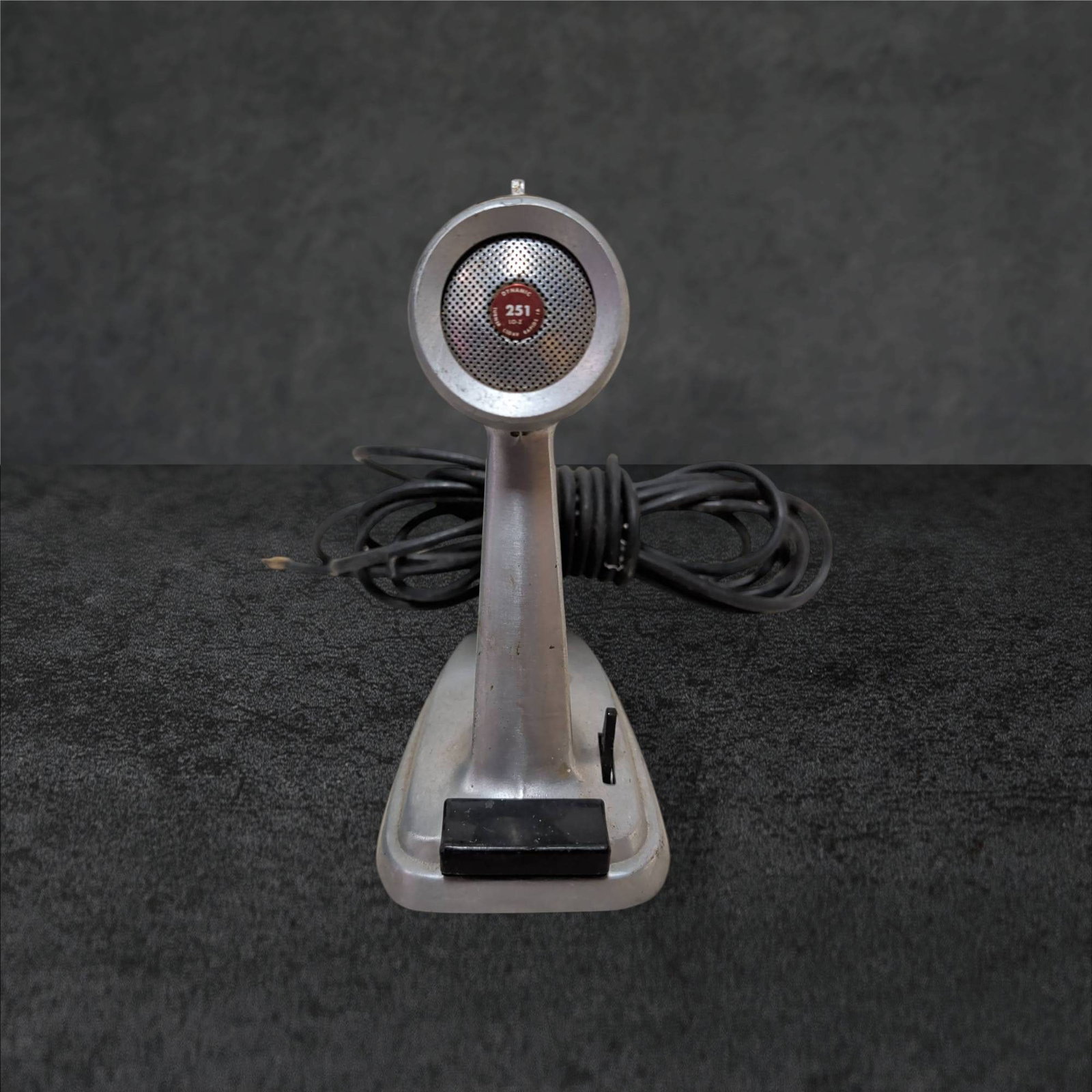 Turner Model 251 Dynamic Microphone with Stand, 8 Inches Tall: Turner Model 251 low-impedance dynamic microphone in a brushed metallic finish, standing 8 inches tall. Integrated stand features base-mounted toggle switch and coiled cord terminating in a 1/4-inch p