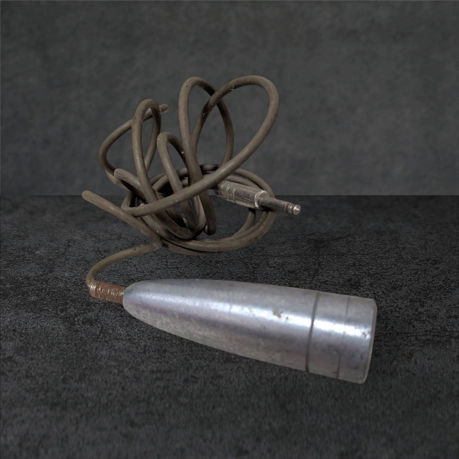 Vintage Corded Microphone, 4.5 Inches Long, Metal Casing: Vintage corded microphone featuring a 4.5-inch metal casing with a sleek conical design. Includes an integrated cord terminating in a 1/4-inch jack plug. The microphone shows signs of use with some su