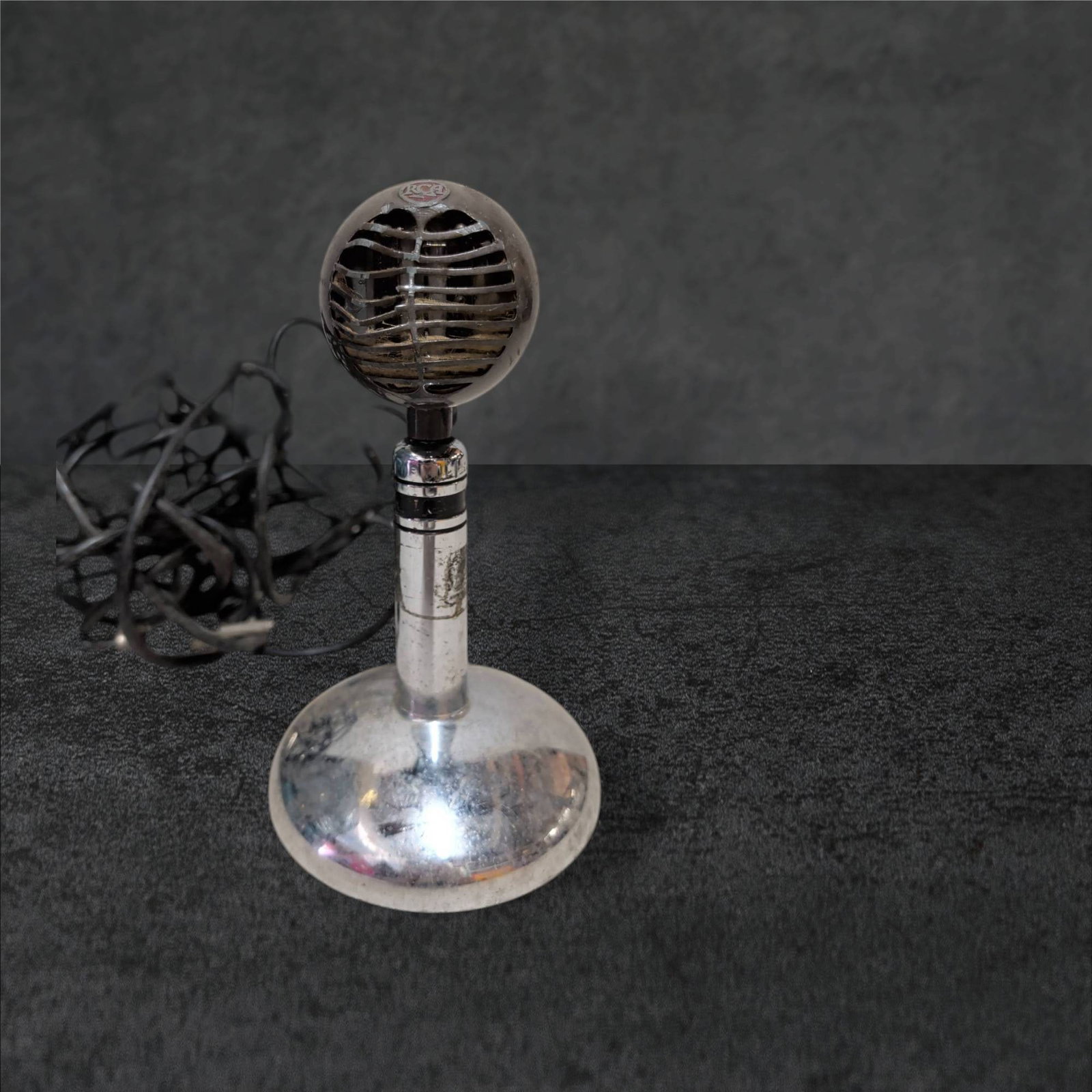 RCA Microphone with Metal Base, 8 1/4 Inches Tall: RCA microphone with a spherical head and a chrome-finished metal base, standing 8 1/4 inches tall. Features the RCA logo on the front grill, which shows signs of wear and damage. Includes a long attac
