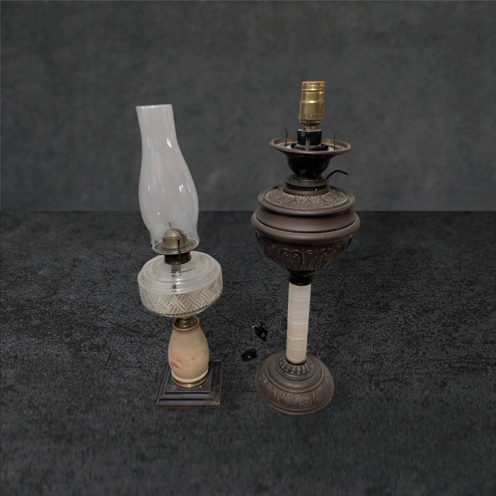 Oil Lamps, Including Modernized Banquet Lamp and Glass Chimney Lamp: Two antique oil lamps comprising of a 22-inch modernized banquet or piano lamp featuring ornate cast metal details, a columnar base, and electrical fittings. The second lamp includes a glass chimney, 