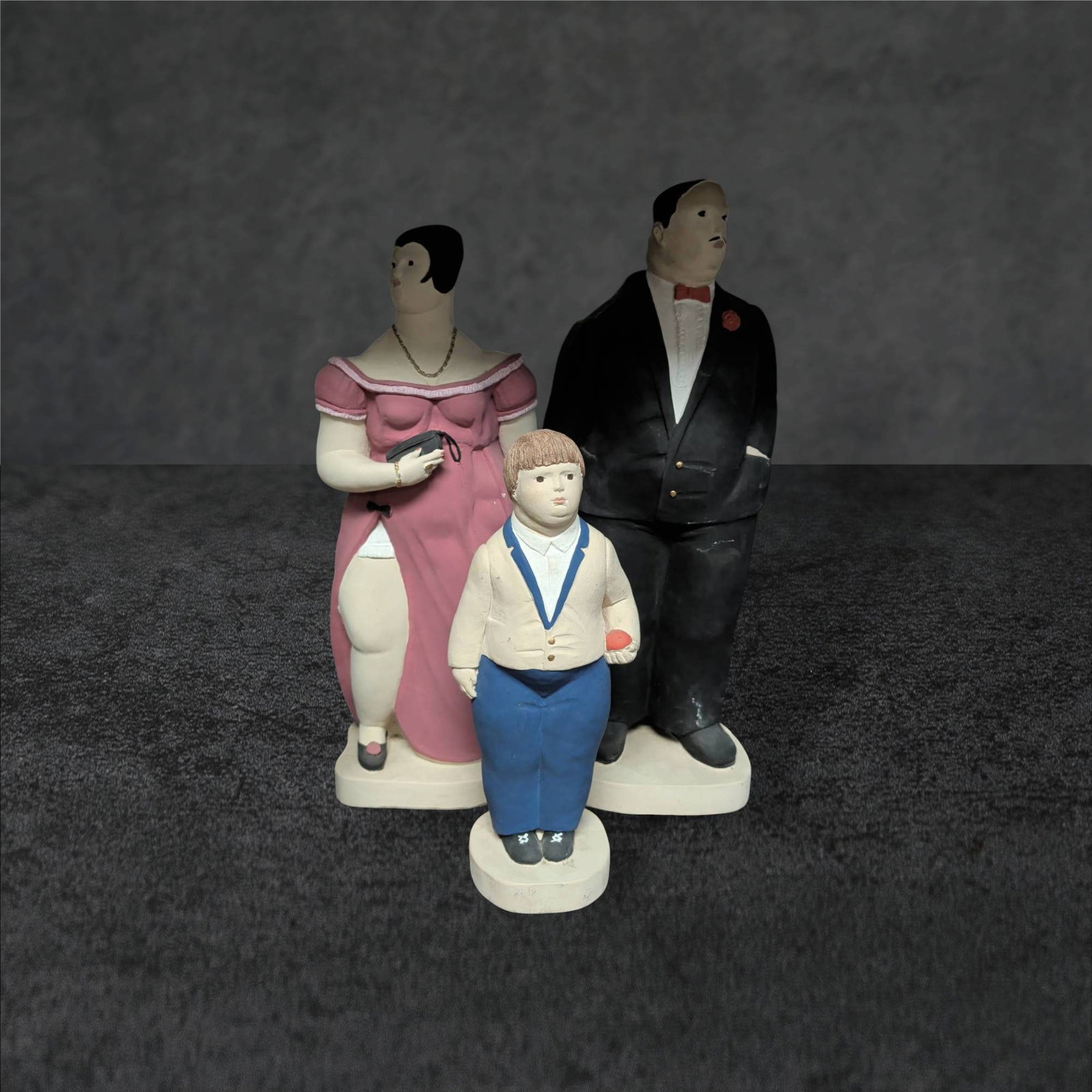 1987 Austin Productions Paolo Grasso Sculpture Trio: Three sculptures by Paolo Grasso for Austin Productions Inc., dated 1987. Includes a man (22.5 in tall), a woman in a pink dress (21 in tall), and a boy with suspenders (14.5 in tall). Made of painted