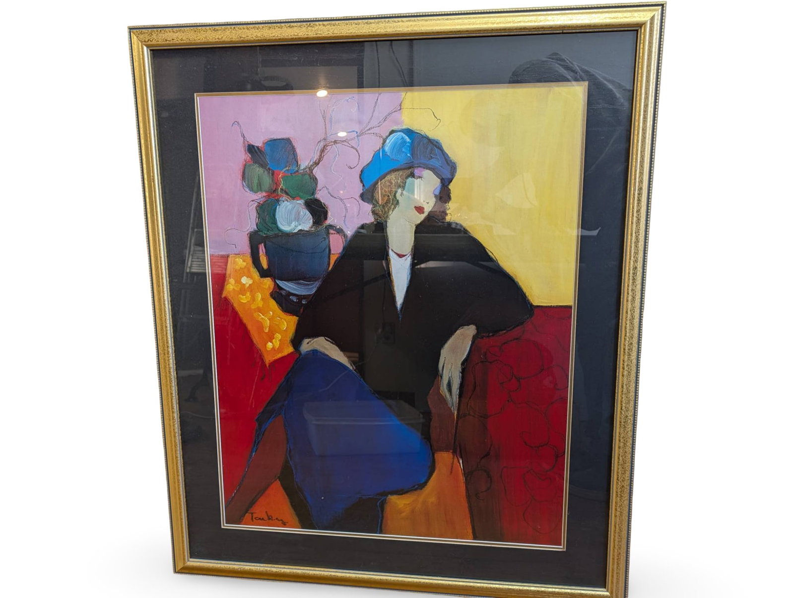 Framed 39 in by 32 in Print of Stylized Seated Woman: Colorful 39 in by 32 in print depicting a stylized seated woman against a vibrant yellow and red background. The figure is adorned with a blue hat and is surrounded by abstract elements, including a v