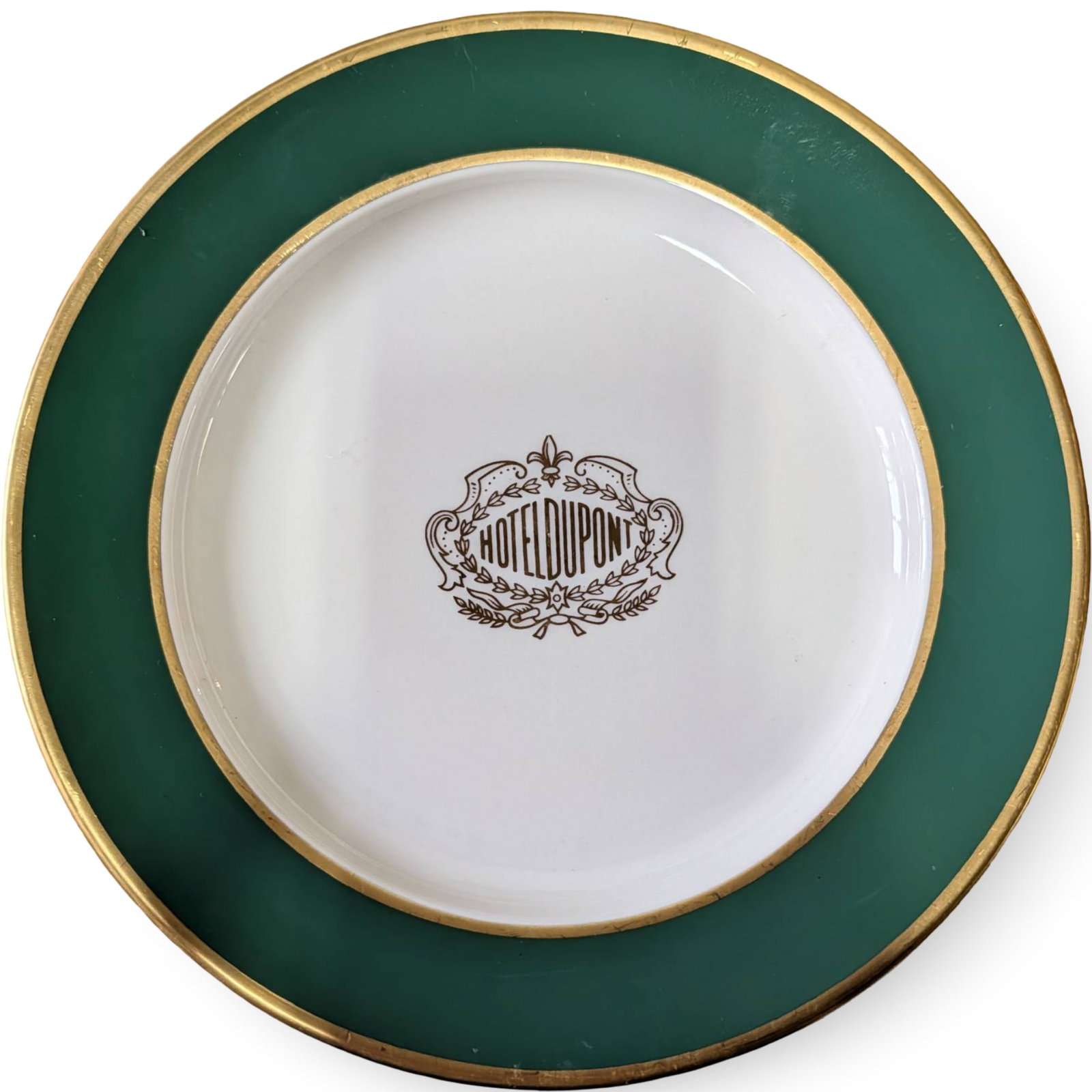 Hotel DuPont Plate by Mayer China, 9-Inch Diameter: A ceramic plate manufactured by Mayer China, featuring the iconic Hotel DuPont logo printed at the center of the dish. The plate has a green border accented with gold trim. The back of the plate bears