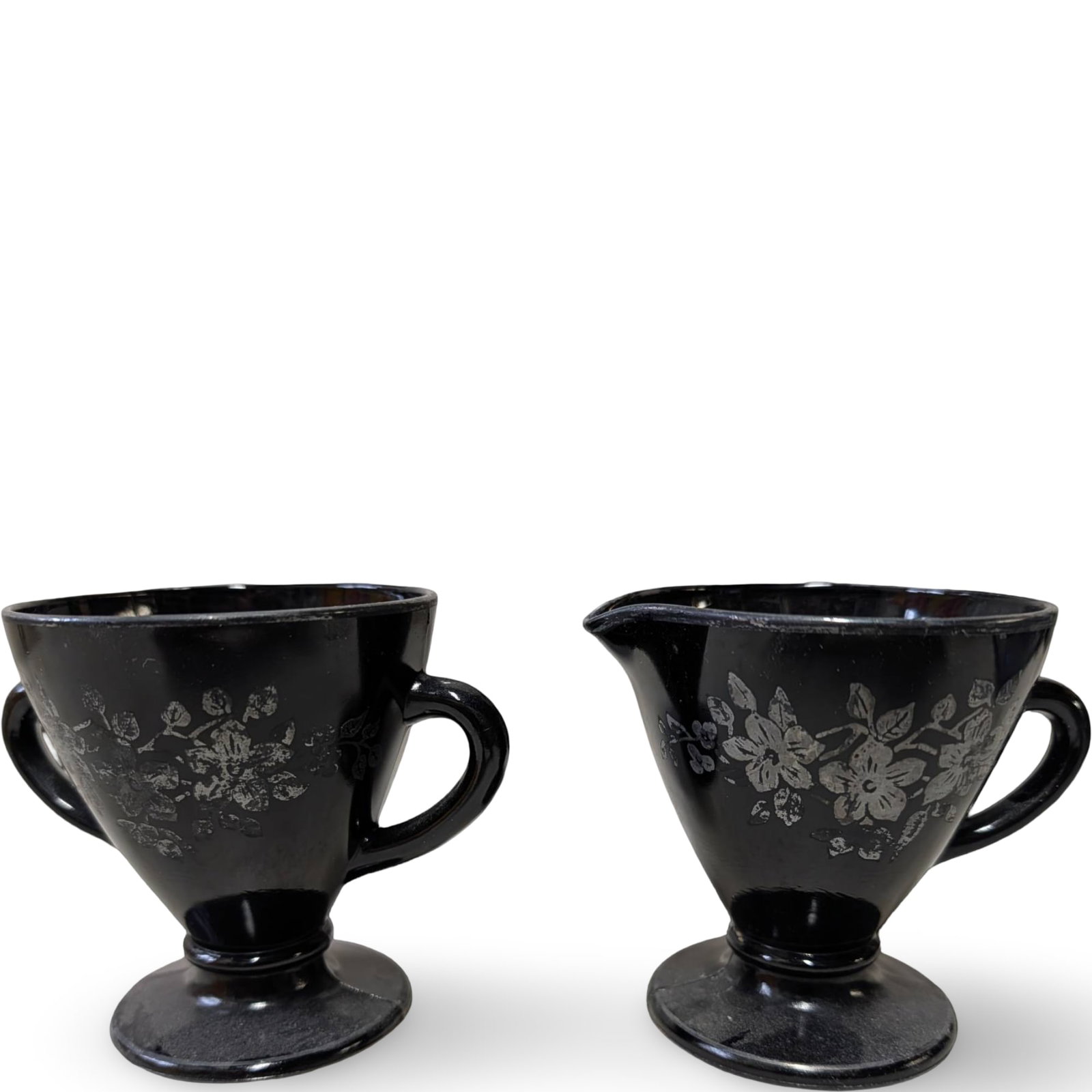 Amethyst Glass Cream and Sugar Set with Silver Overlay: Cream and sugar set crafted from amethyst-colored glass, featuring decorative silver overlay floral motifs. Both pieces are approximately 3 1/2 inches tall and 4 inches in diameter. The cream pitcher 