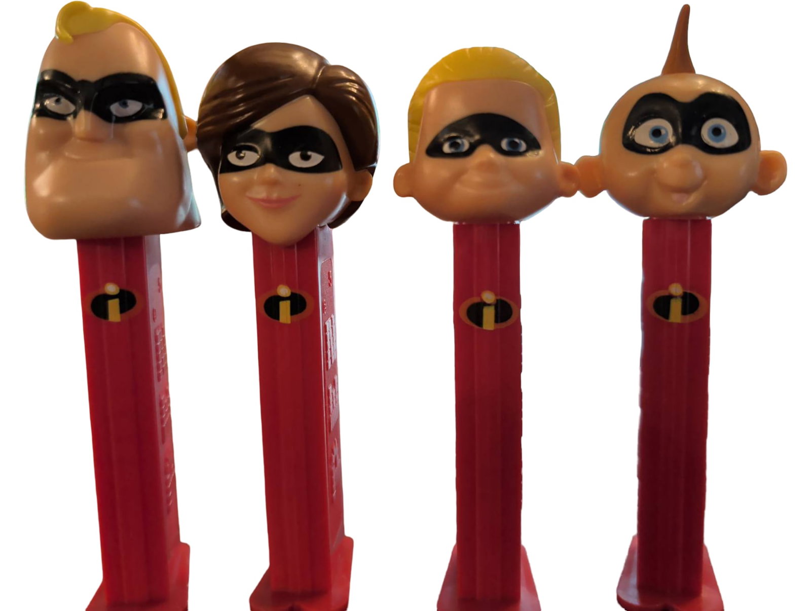 Four Themed PEZ Dispensers with Character Heads: Four PEZ candy dispensers featuring character heads. Each dispenser has a red body and a unique character head, styled after superhero characters wearing masks. The dispensers are functional with hing