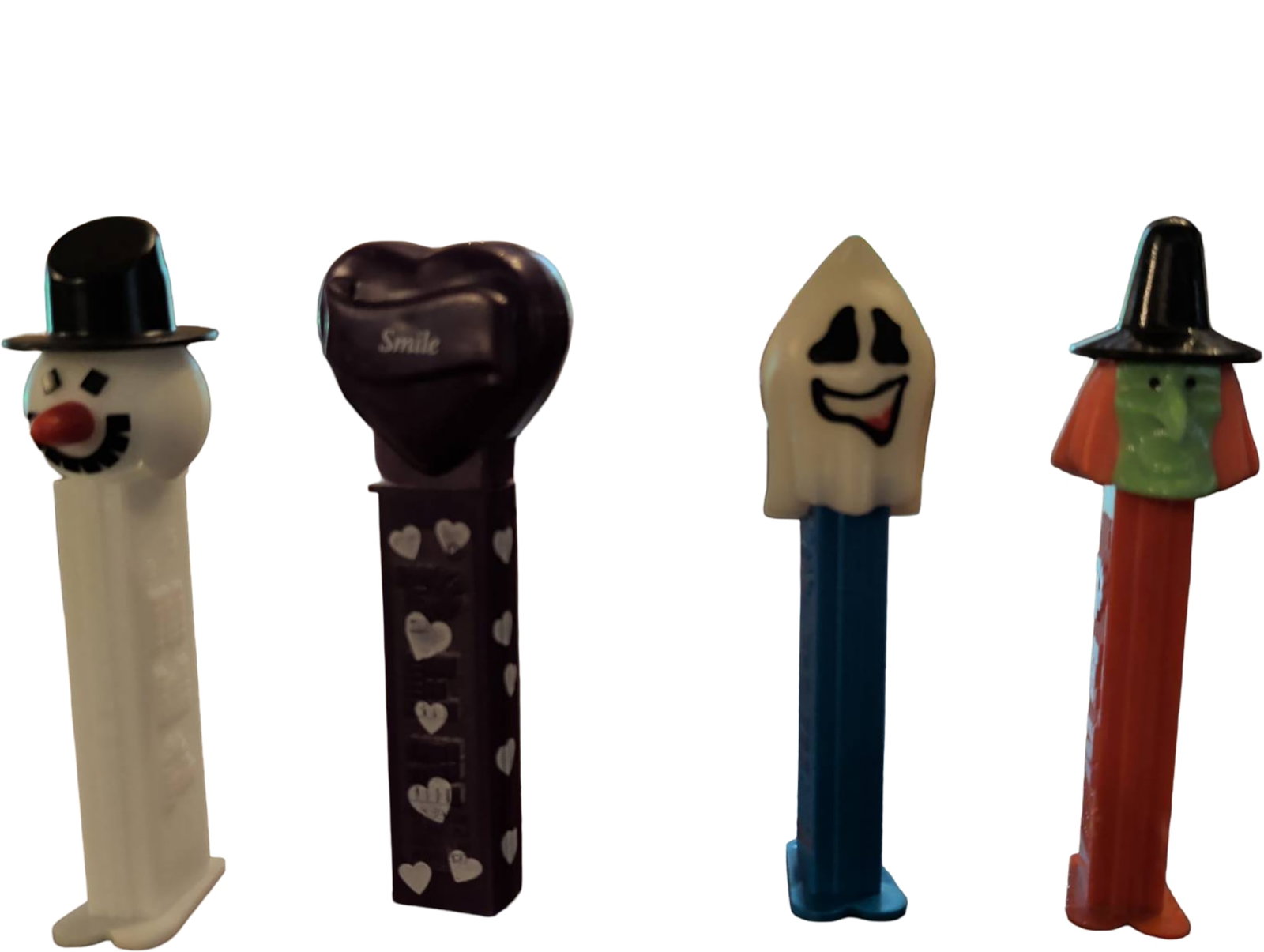 Four Themed PEZ Dispensers: Snowman, Valentine, Ghost, and Frankenstein: Four PEZ dispensers featuring themed designs: a snowman with a black hat, a purple Valentine heart with white accents, a ghost with a blue base, and a Frankenstein figure with a black hat. Each dispen