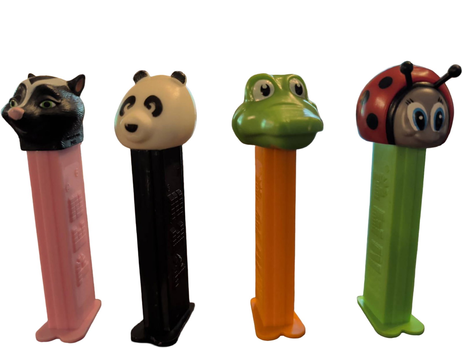 Four Animal-Themed PEZ Dispensers: Four PEZ candy dispensers featuring animal-themed heads: a raccoon (pink base), panda (black base), frog (orange base), and ladybug (green base). Made of plastic, these dispensers are functional and d