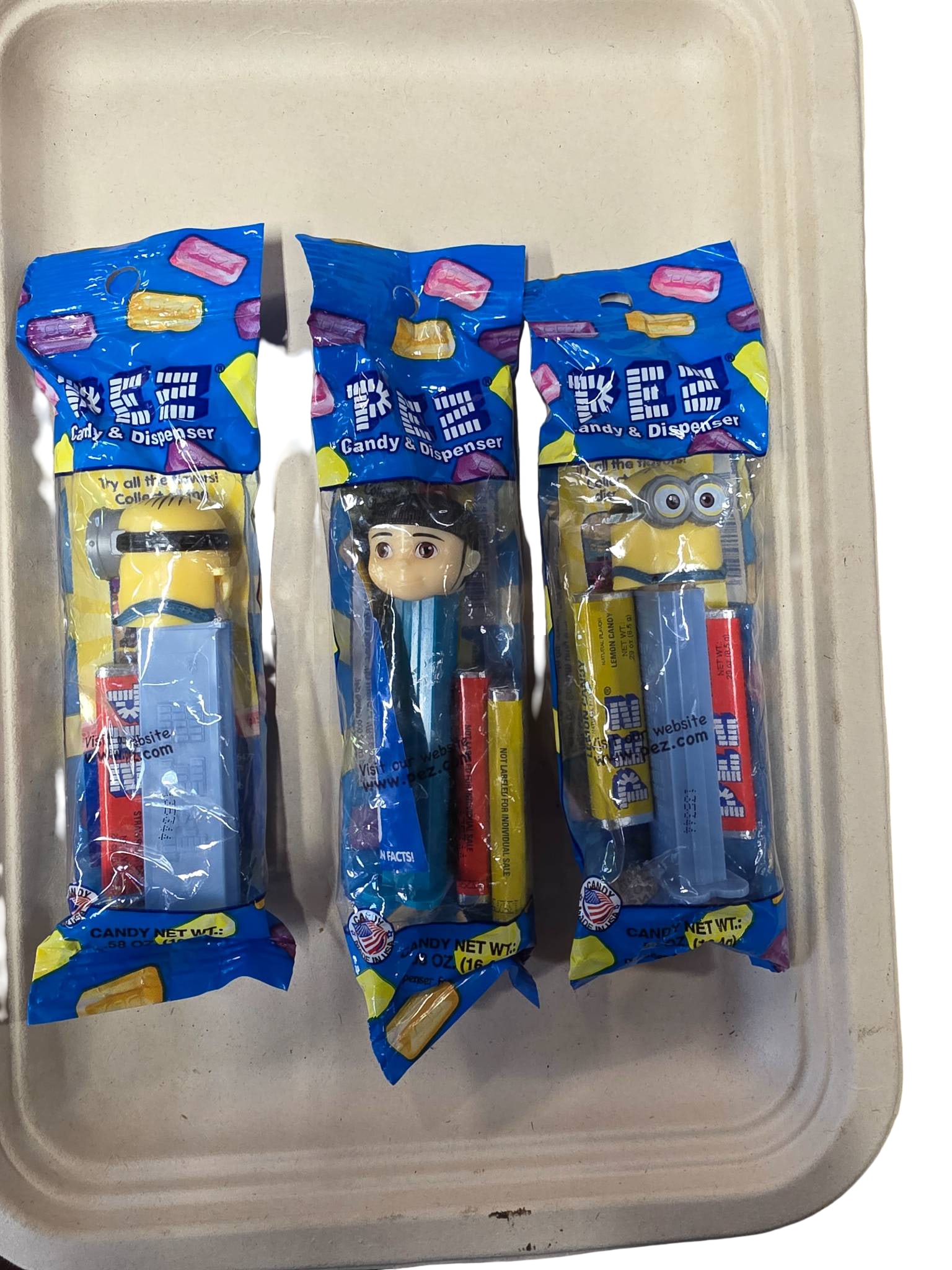 Three PEZ Dispensers in Original Packaging Featuring Minions and Generic Characters: Three PEZ candy dispensers, each in unopened original packaging. The designs include two Minions character-themed dispensers and one featuring an unknown generic character. Packaging includes attached