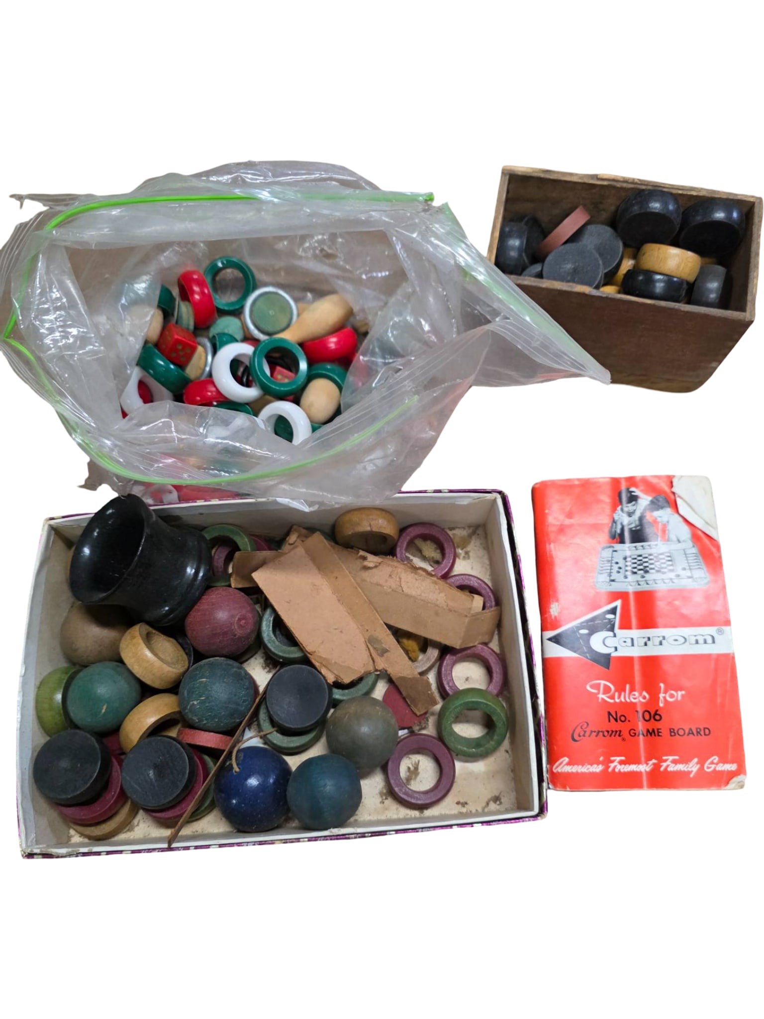 Carrom Game Board Pieces with Instruction Manual: Carrom game board pieces, including discs in various colors, strikers, and accessories. Includes an original Carrom red instruction manual and storage containers. Pieces exhibit signs of wear