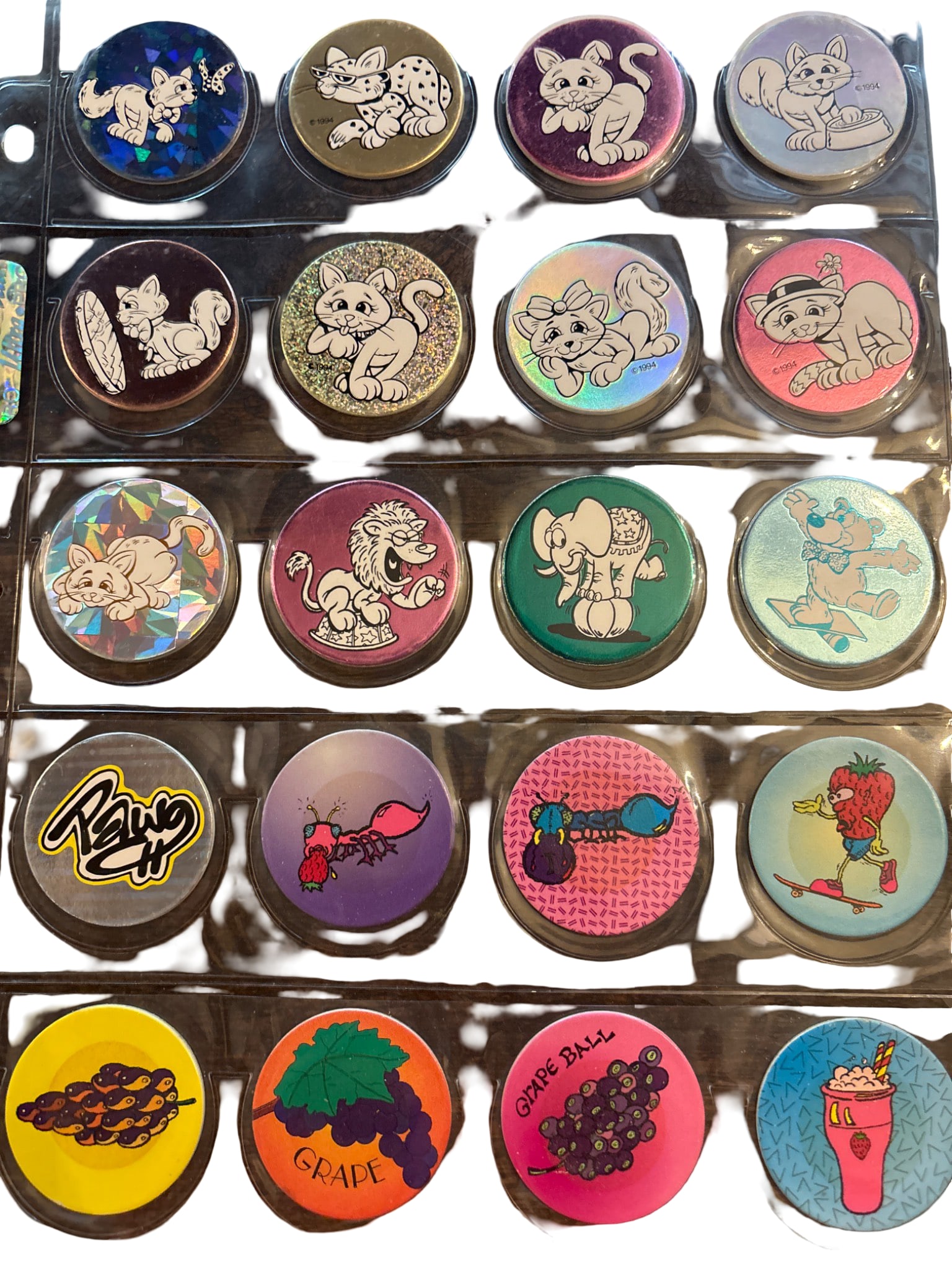 Vintage Pog Milk Caps Featuring Cat and Fruit Designs: Collection includes 20 vintage Pog milk caps with various printed designs, including cartoon-style cats, fruit, and playful graphics. Caps are stored in a plastic sheet with 20 slots, 18 of which are 