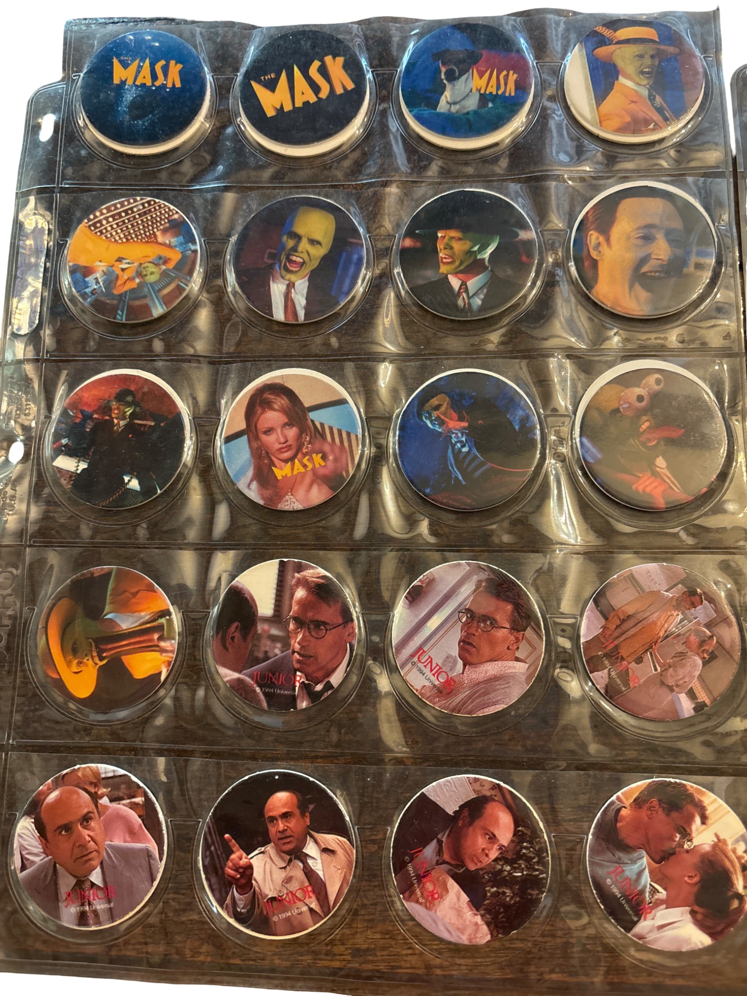 Collectible movie Pogs: Pogs featuring imagery and characters from 'The Mask', ‘Junior’, ‘ Dumb and Dumber’ and 'Richie Rich' movies, arranged in a plastic binder with individual slots. Graphics depict scenes and cha