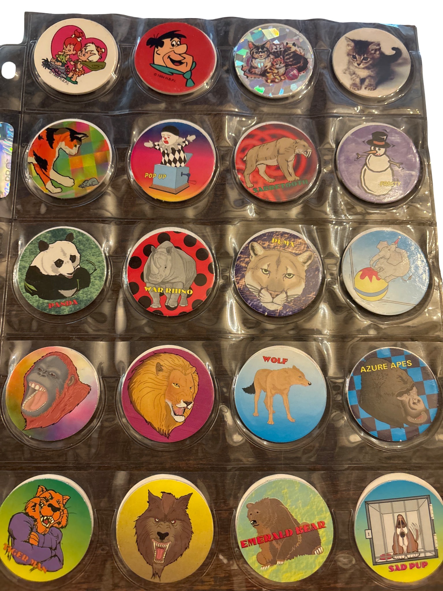 Pog Milk Caps with Animal and Cartoon Designs: Pog milk caps stored in plastic sleeve pages. Designs feature a variety of animal, cartoon, and fantasy themes, including lions, wolves, swans, and characters. The collection includes holographic and 