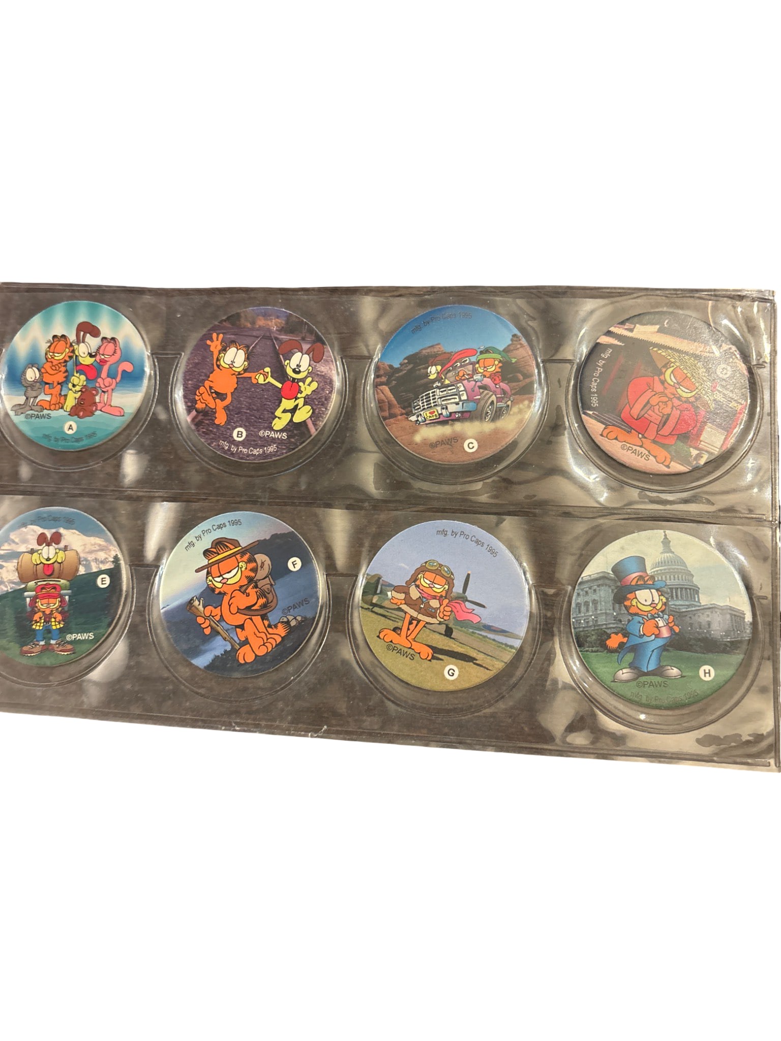 8 Pog A-H Collectible Discs Featuring Garfield Designs: 8 collectible pog discs identified as Pog A-H, each featuring colorful Garfield-themed illustrations. The discs are encased in transparent plastic sleeves for protection. Designs include various scene