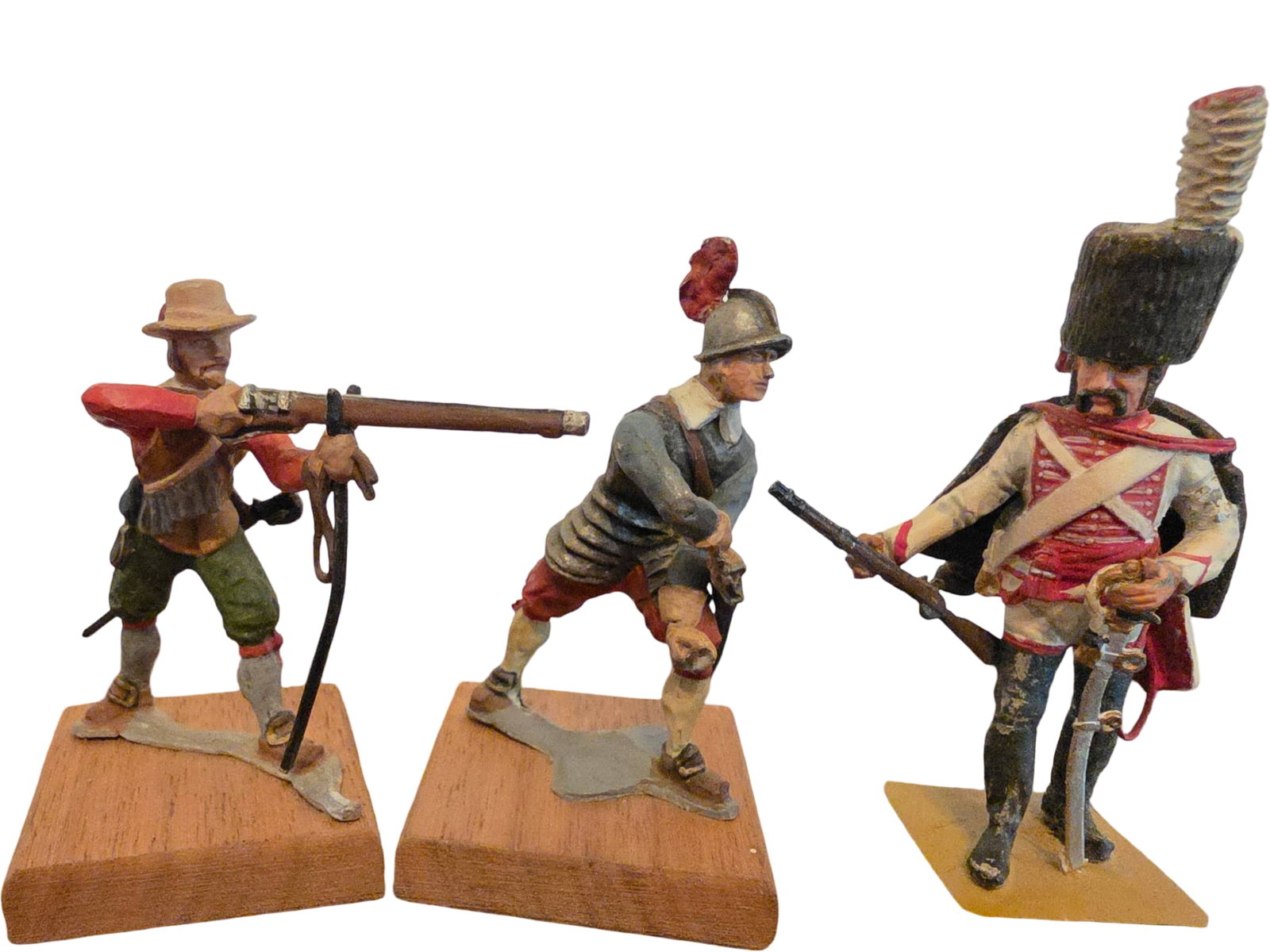 Three Painted Metal Military Figurines on Bases: Three detailed painted metal military figurines representing historical soldiers, mounted on wooden and flat bases. Includes one with a musket and hat, another in armor with a sash, and one in a tall