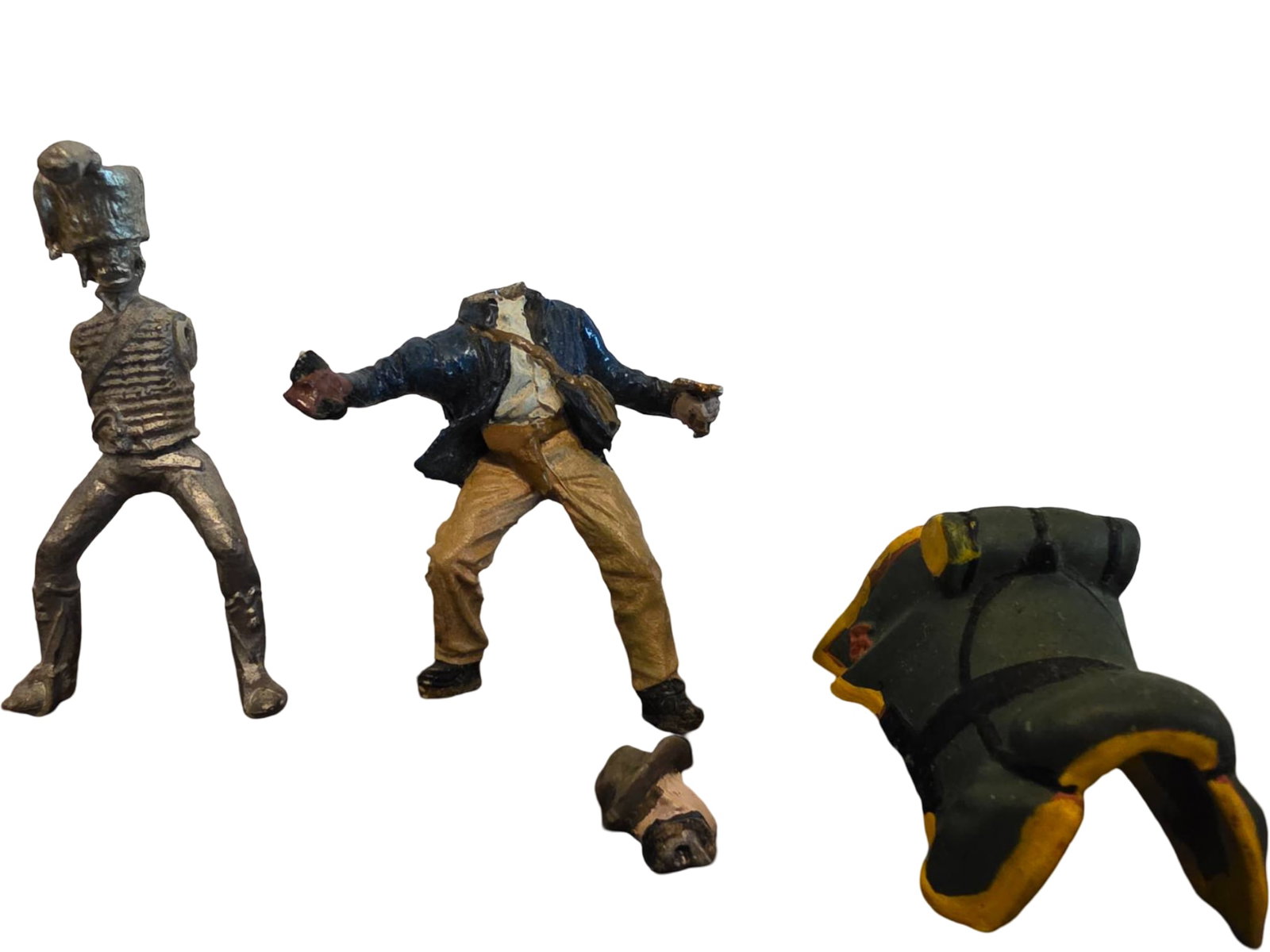Three Painted and Unpainted Military Figurines with Detached Parts: Three military-themed figurines: one unpainted metal soldier, one painted soldier with detached head, and one painted pack. The items show signs of wear, including missing or detached parts, such as