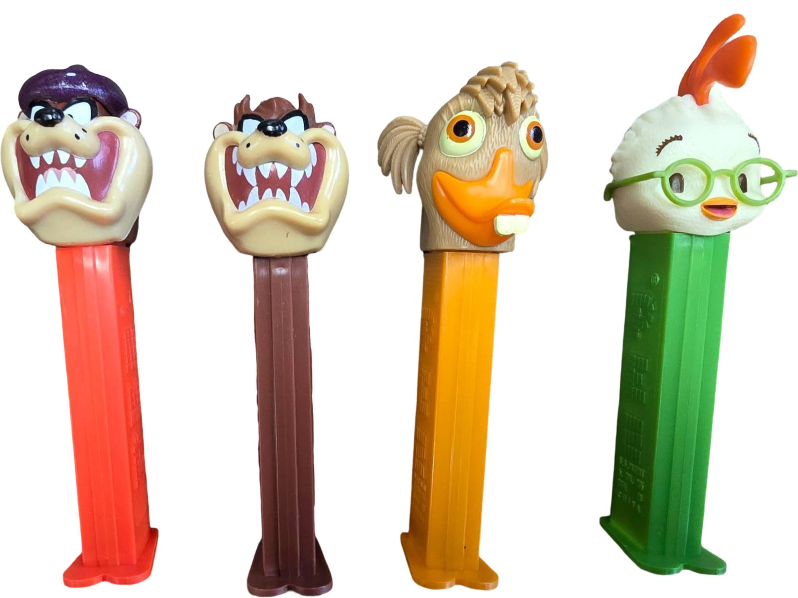 Four PEZ Dispensers Featuring Taz and Chicken Little Characters: Four PEZ candy dispensers, including two depicting Taz from Looney Tunes and two depicting Chicken Little characters. Each brightly colored dispenser features a character head atop a plastic base. Lig