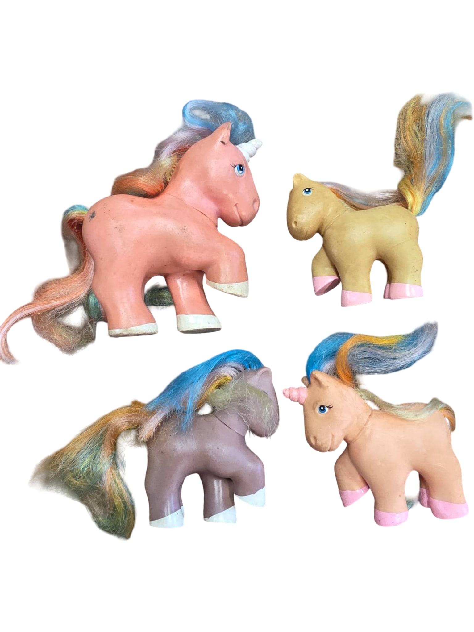 Four Vintage Plastic Toy Unicorns with Multicolored Hair: Four small plastic toy unicorns featuring multicolored synthetic hair and painted facial details. Each unicorn displays unique coloration of the body and hair, with some showing wear consistent with h