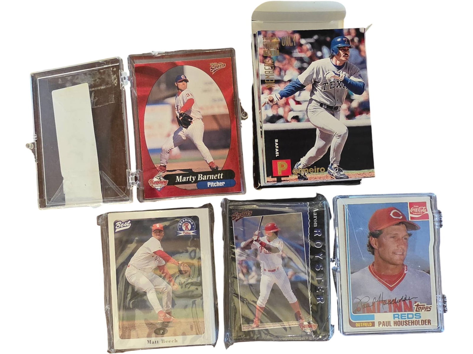 Baseball Trading Cards in Protective Cases: Group lot of baseball trading cards, including multiple cards displayed in protective plastic cases and loose cards arranged in stacks. Various players and teams featured, with a mix of branded card d
