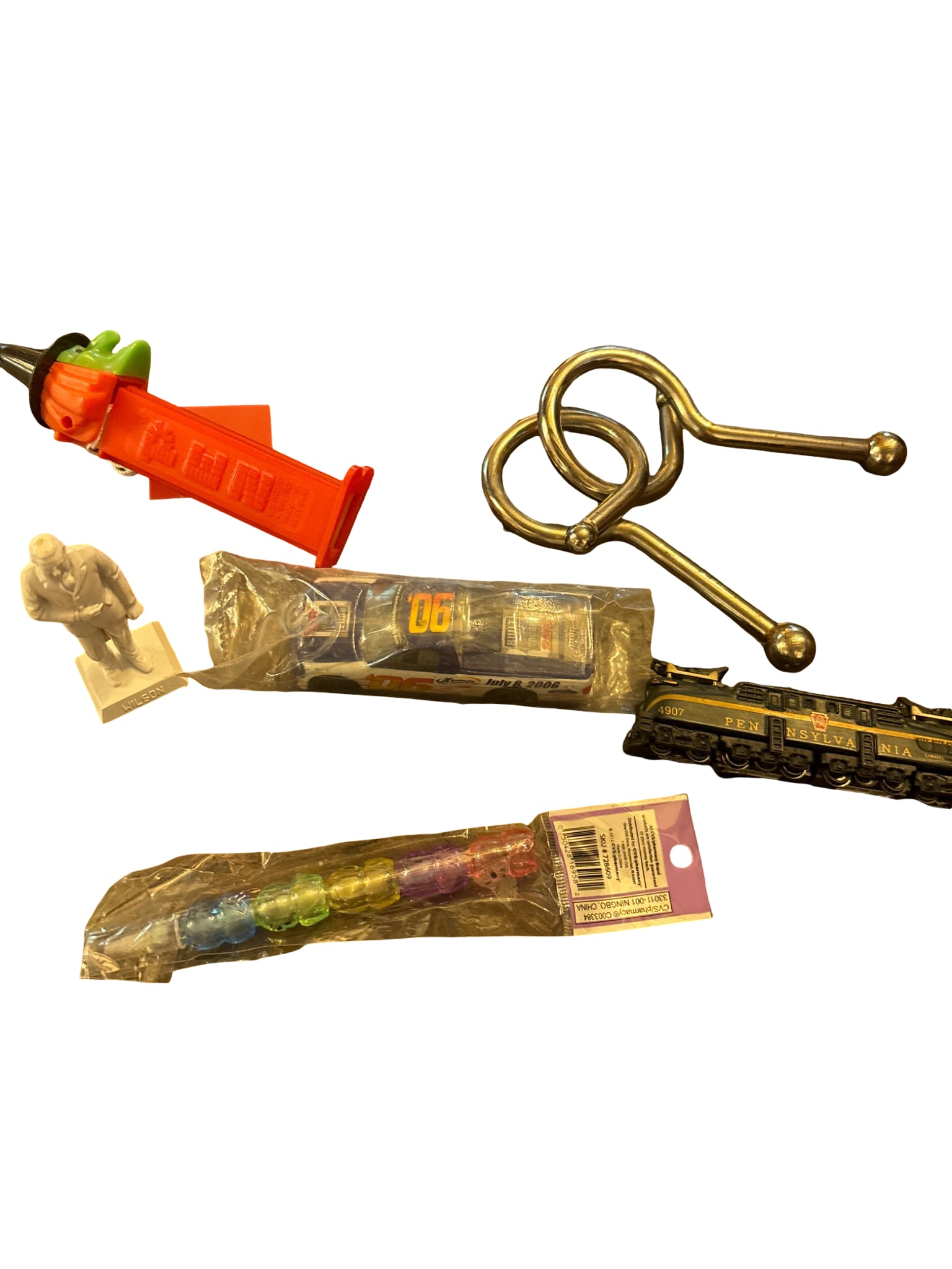 Collectible Items: PEZ Dispenser, Miniature Train, NASCAR Car, Puzzle, and Wilson Figure: Collectible items, including a red witch-themed PEZ dispenser, a die-cast Pennsylvania Railroad miniature train model #4907, a packaged NASCAR collectible car marked 'July 8, 2006' and '#06,' a small