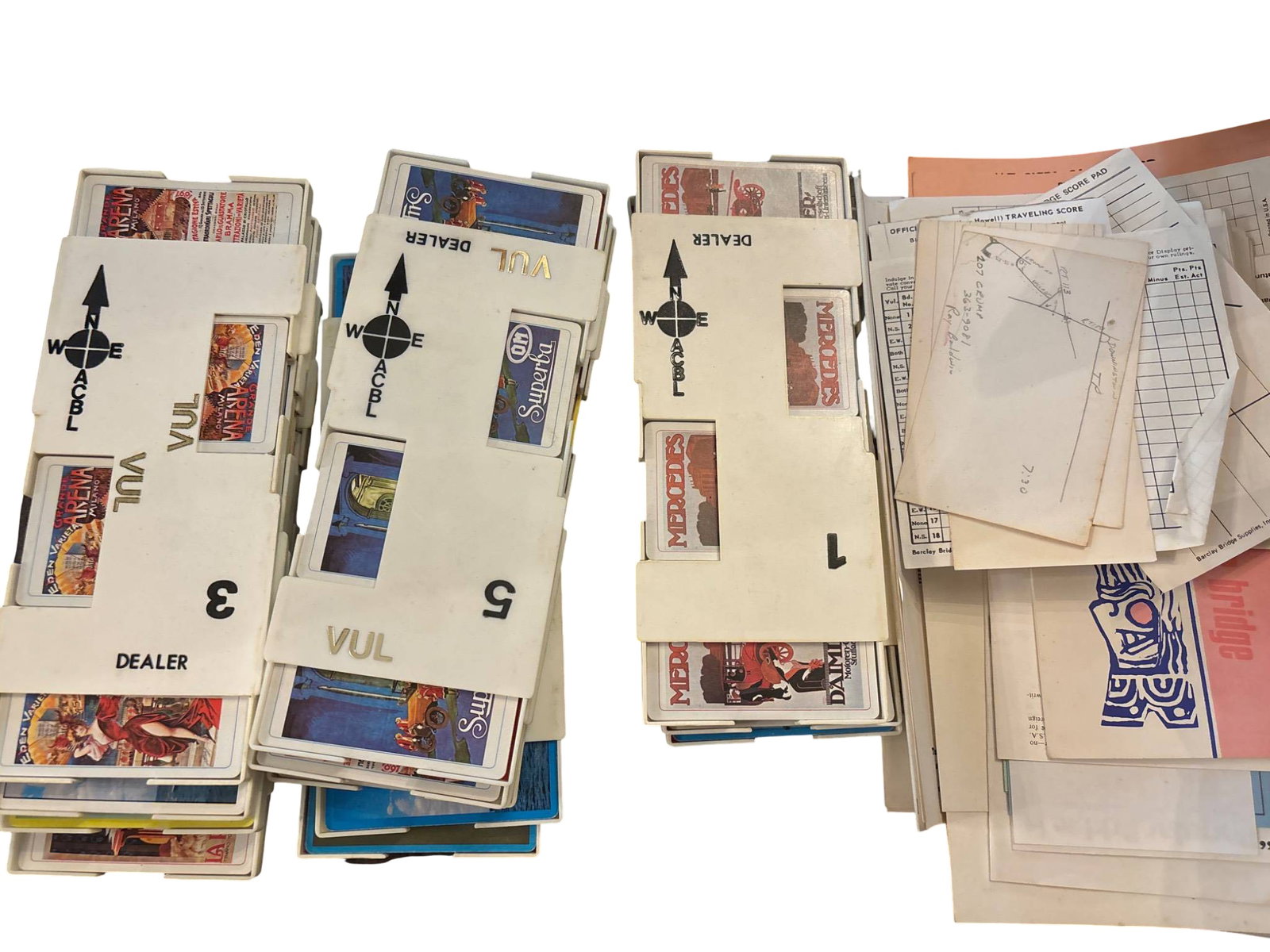 Vintage Bridge Playing Cards with Instructional Materials and Score Sheets: 16 decks of vintage bridge playing cards in slipcases labeled with 'Dealer' and 'VUL.' Cards feature a variety of designs, with accompanying instructional materials, score sheets, and bridge puzzles.