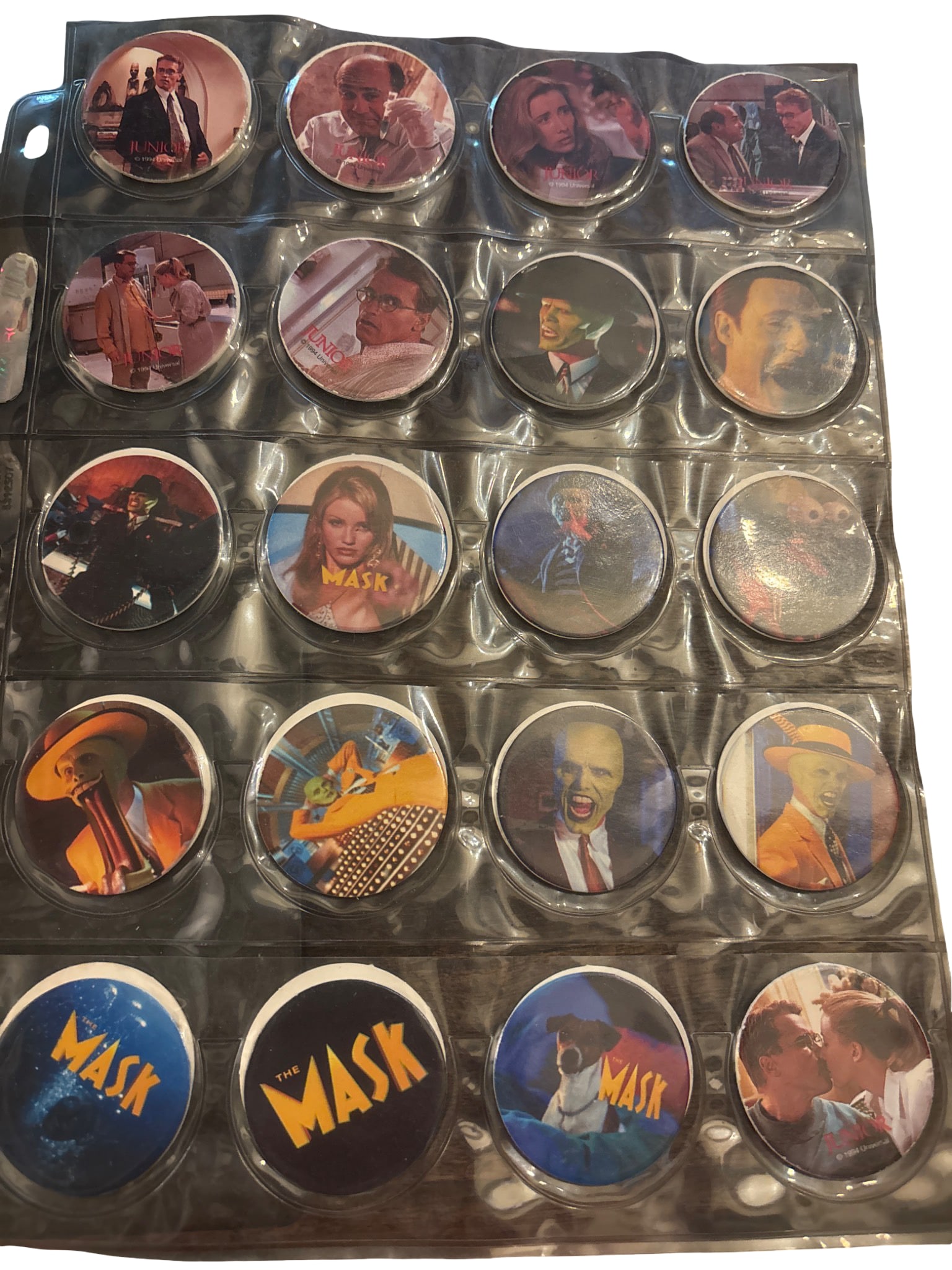 Themed Pog Milk Caps Featuring Iconic 1990s Movie Characters: Themed Pogs (milk caps) in protective sleeves. Features imagery from 1990s movies such as 'The Mask,' 'Richie Rich,' and others. Each Pog is printed with characters, logos, and scenes from the films. 