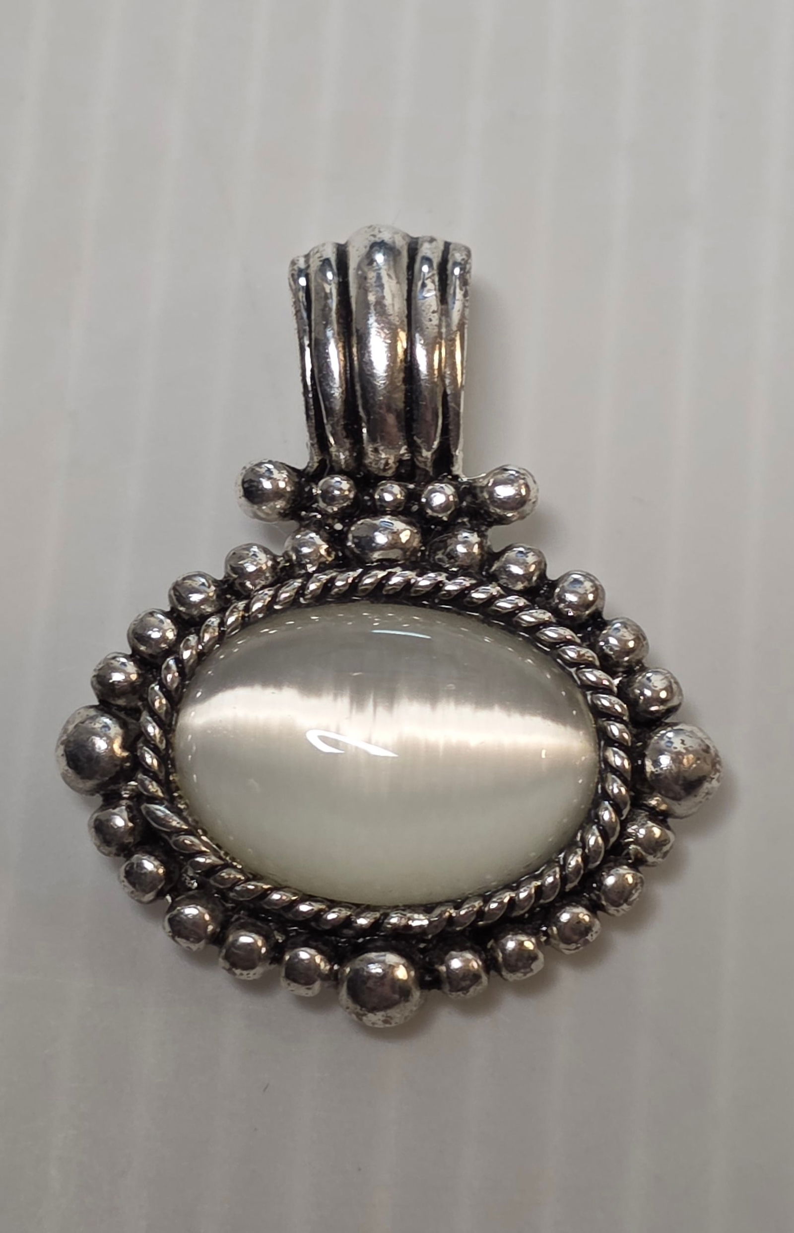 Vintage Style White Moonstone Cabochon Pendant Silver Tone Ornate Frame: Vintage inspired pendant featuring an oval white moonstone appearance cabochon set in ornate beaded and rope detail frame. Silver tone metal. No metal purity marks observed. Non magnetic under testing