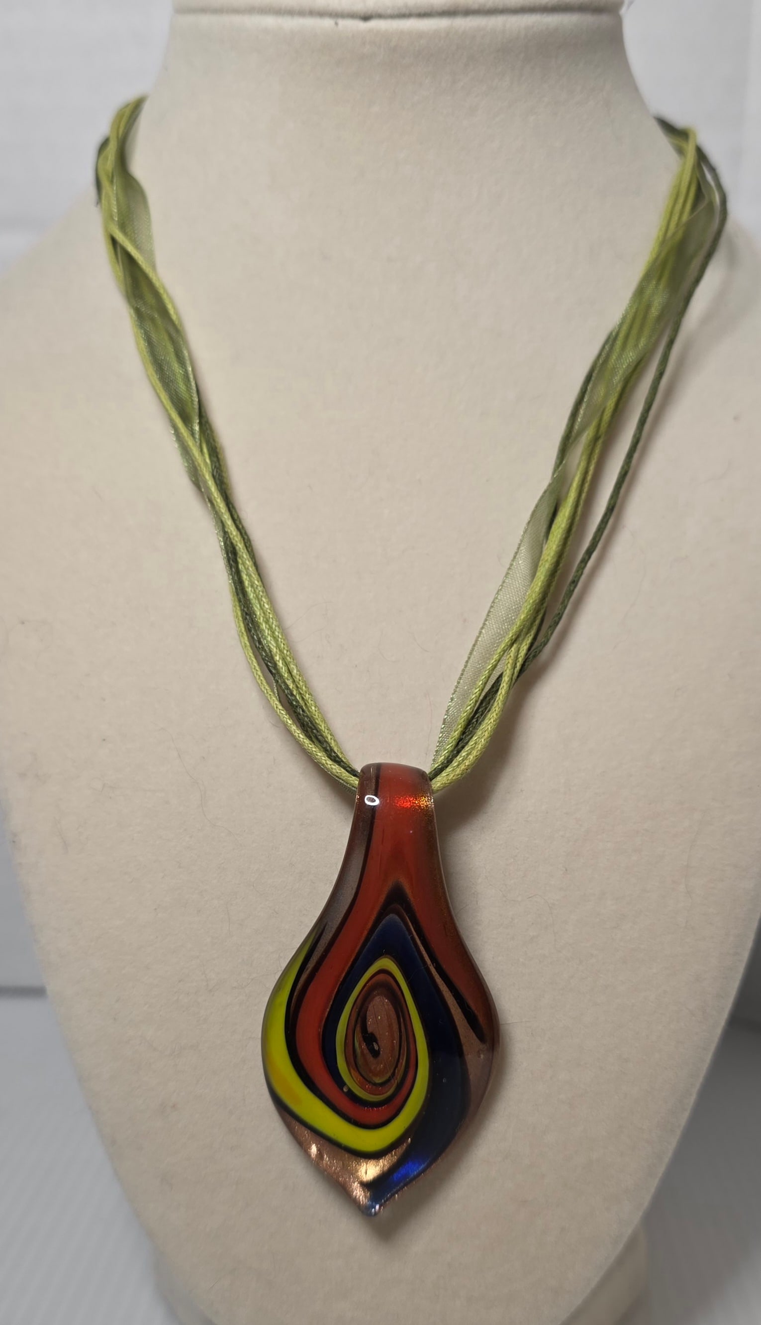 Handblown Art Glass Pendant Necklace Multicolor Teardrop Fabric Cord: Handblown art glass pendant in elongated teardrop form featuring layered multicolor design with copper tone shimmer and deep blue reverse. Suspended on multi strand green fabric cord necklace with lob