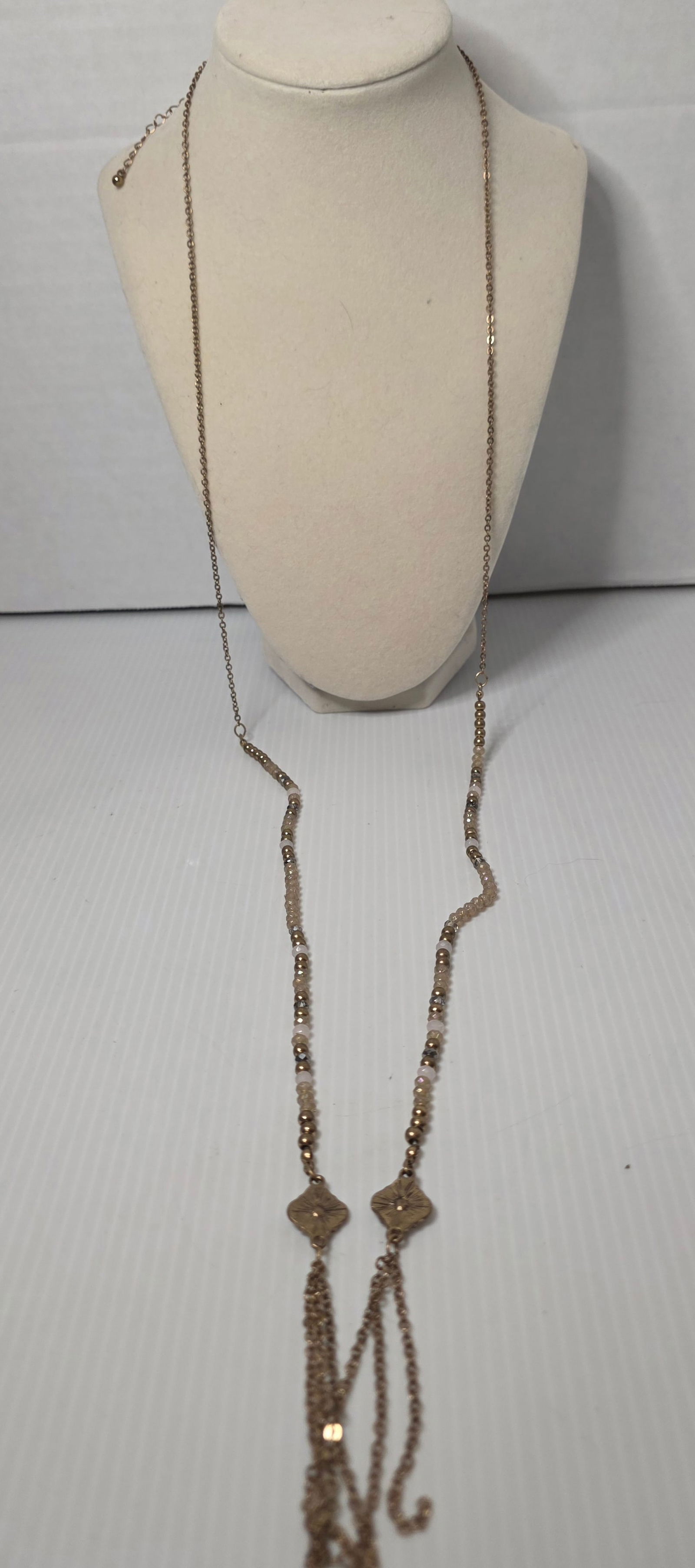 Long Beaded Tassel Necklace Gold Tone Rhinestone Accent: Long gold tone necklace featuring mixed glass and bead elements with faceted crystal style accents and decorative clover shaped rhinestone connectors. Double tassel chain drops at center. Adjustable e