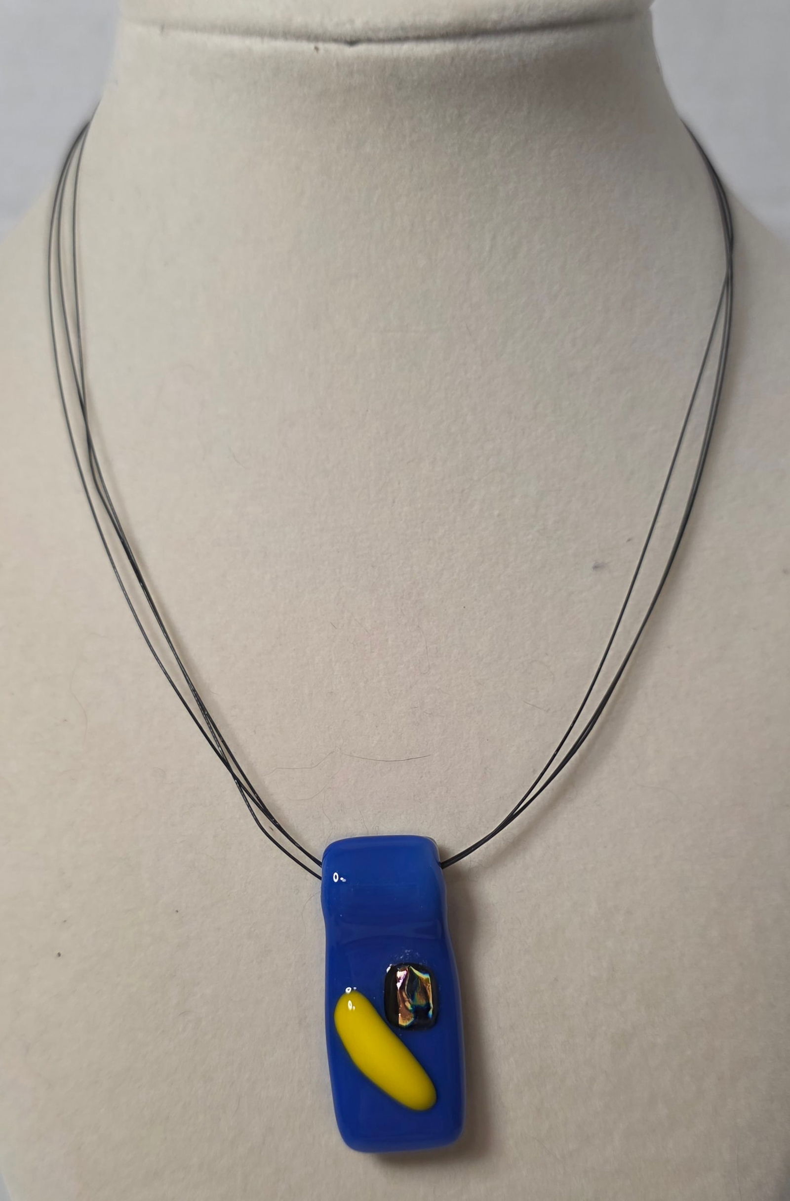Modern Blue Glass Pendant Necklace Multi Strand Cord: Modern statement necklace featuring rectangular cobalt blue glass pendant with applied yellow accent and iridescent detail. Pendant suspended on multiple black cord strands with lobster clasp closure.