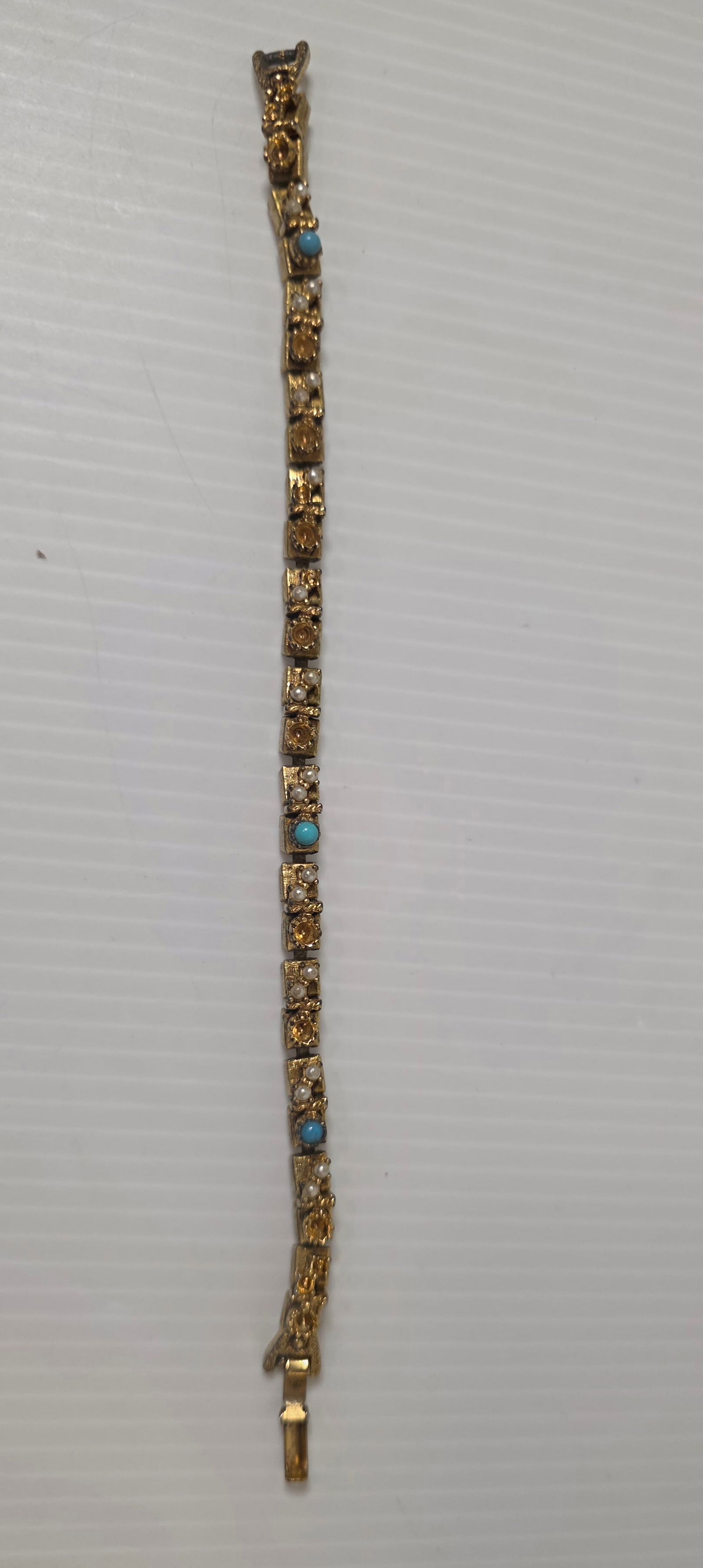 Vintage Gold Tone Link Bracelet Faux Pearl Blue Accent: Vintage gold tone link bracelet featuring textured rectangular links with small faux pearls, amber tone rhinestones, and blue accent stones. Decorative fold over clasp. Measures approximately as shown