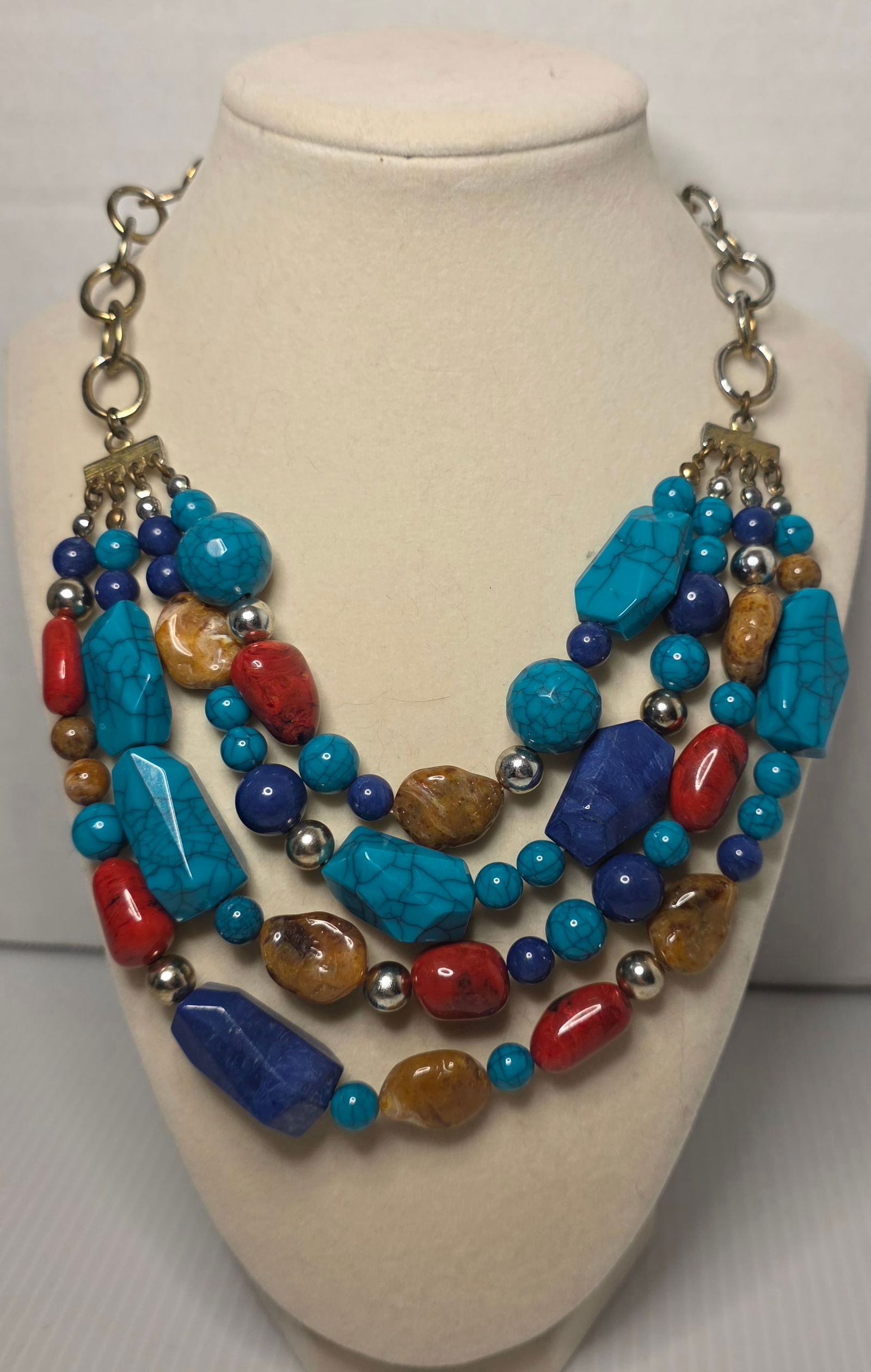 Multi Strand Turquoise Coral Lapis Style Bead Statement Necklace: Multi strand statement necklace featuring turquoise color beads with veining, red coral color beads, blue lapis style beads, brown stone beads and silver tone spacer beads. Large link chain extension