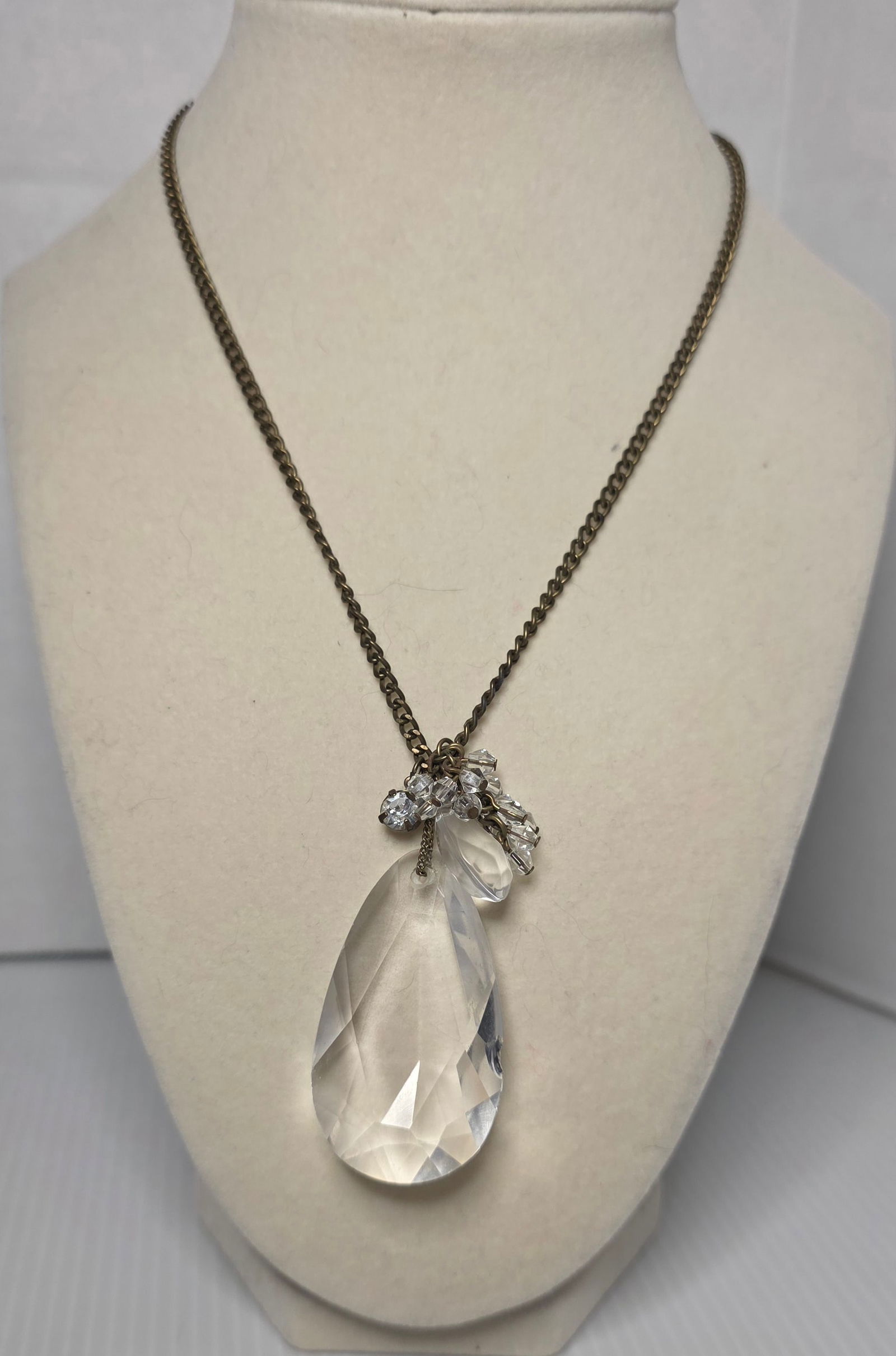 Bronze Tone Chain Necklace Large Faceted Teardrop Pendant: Bronze tone chain necklace featuring a large faceted clear teardrop pendant with additional clear bead accents. Lobster clasp with extender chain. Measures approximately 18 inches with extender as sho