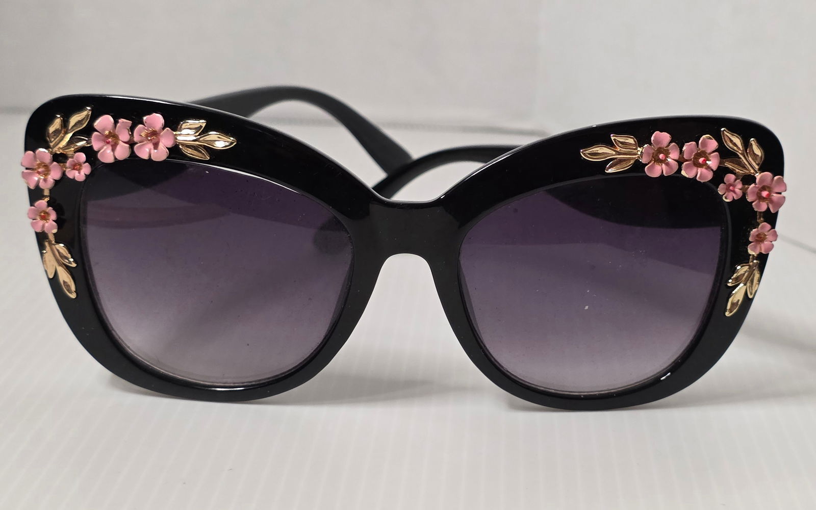 Womens Large Black Floral Enamel Sunglasses Oversized: Womens oversized black sunglasses with pink enamel floral and gold tone leaf embellishments on front corners and temples. Dark gradient lenses. Unmarked brand.Measures approximately 6 inches across fr