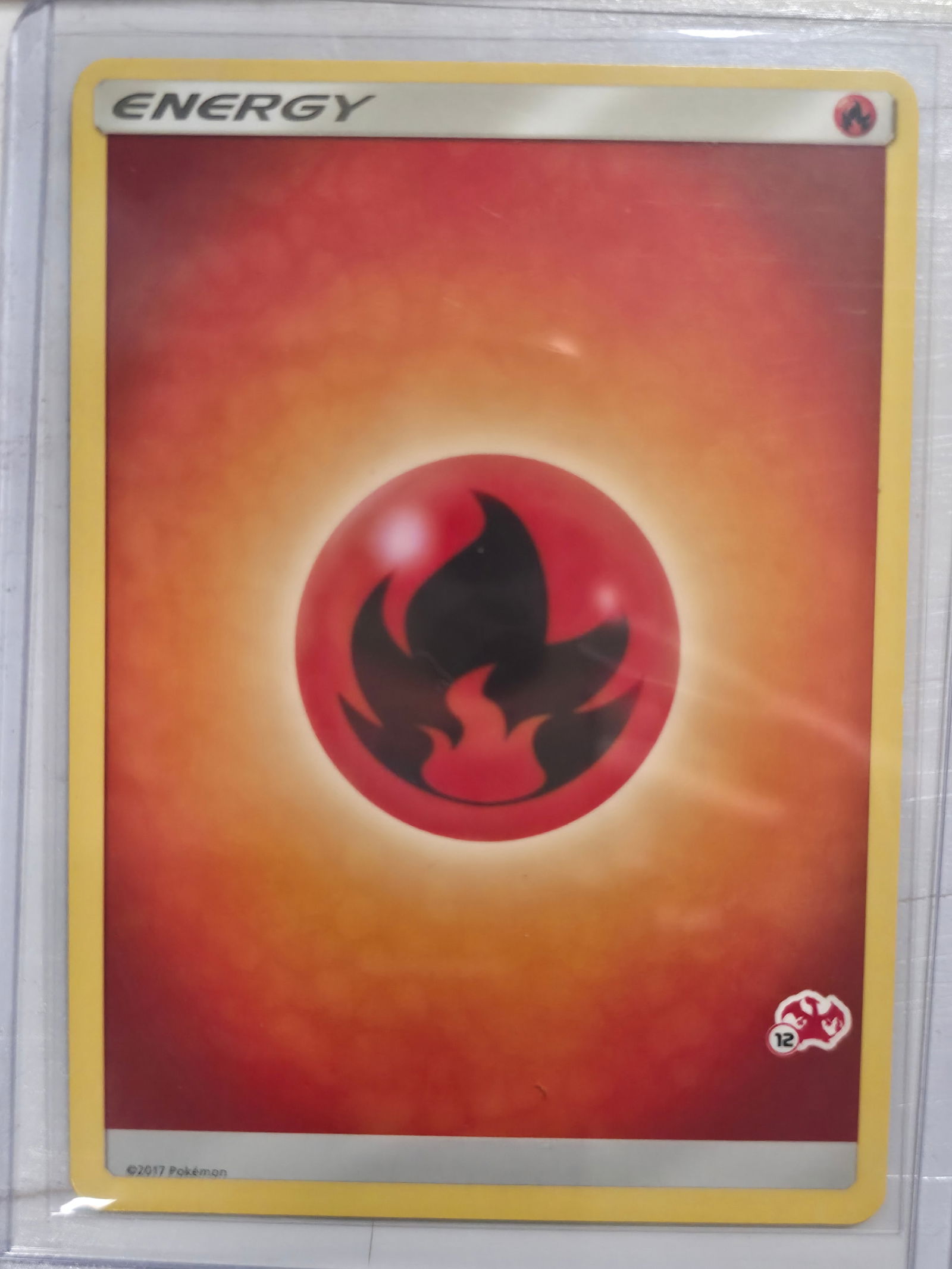 2017 Fire Energy Sun and Moon Promo 12/12 Common: Basic Fire Energy card. 2017 Sun and Moon era print. 12/12 variant with set stamp symbol at lower right. Standard non holo finish. 2017 Pokemon. Preowned card stored in penny sleeve and top loader.