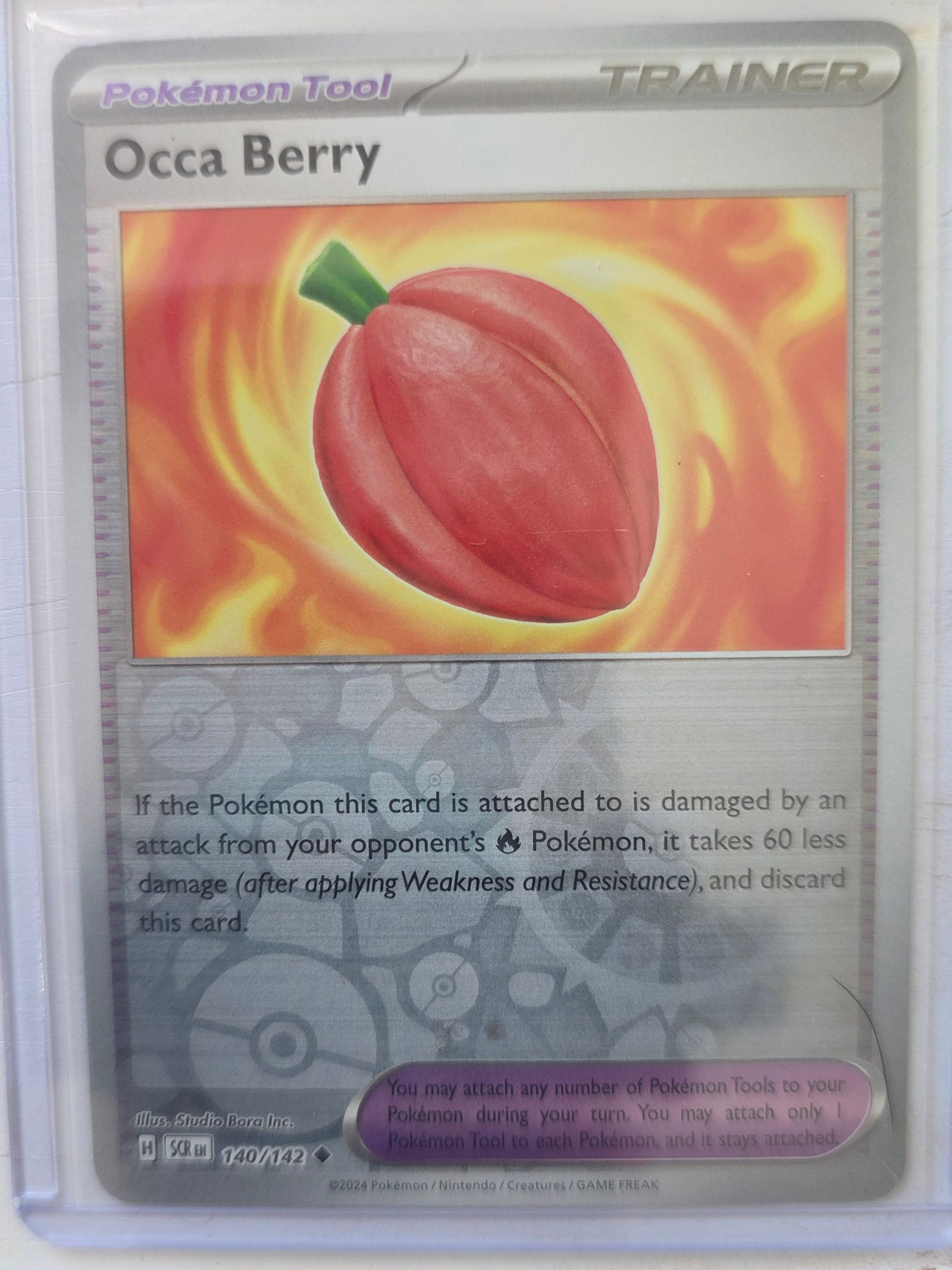 2024 Occa Berry 140/142 Reverse Holo: 2024 Occa Berry Trainer Pokemon Tool card 140/142. Reverse holo foil pattern across card surface with non holo artwork box. Red berry artwork on flame background. Preowned card stored in penny sleeve
