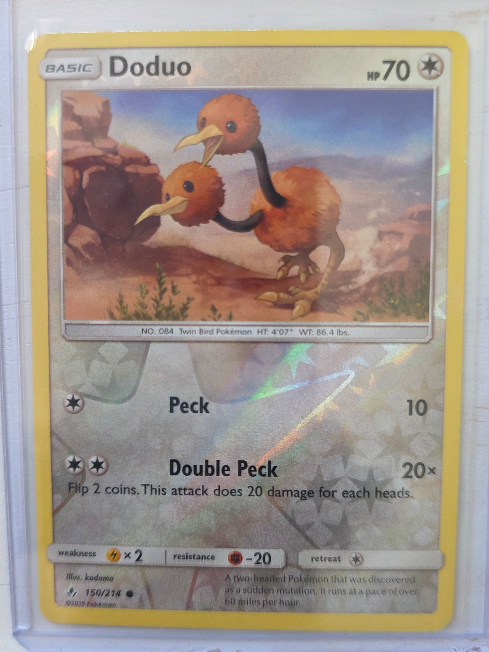 2019 Doduo 150/214 Reverse Holo: 2019 Doduo Basic card 150/214. 70 HP Colorless type. Reverse holo foil pattern across card surface with non holo artwork box. Peck 10. Double Peck 20x. Preowned card stored in penny sleeve and top loa