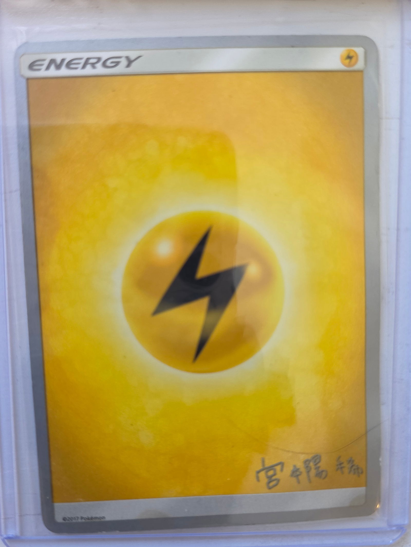 2017 Lightning Energy Sun & Moon Promo Signed Pokemon Card: 2017 Pokemon Lightning Energy card with printed signature artwork used in the Sun & Moon era promotional releases. Standard basic energy card design. Card stored in penny sleeve and top loader.