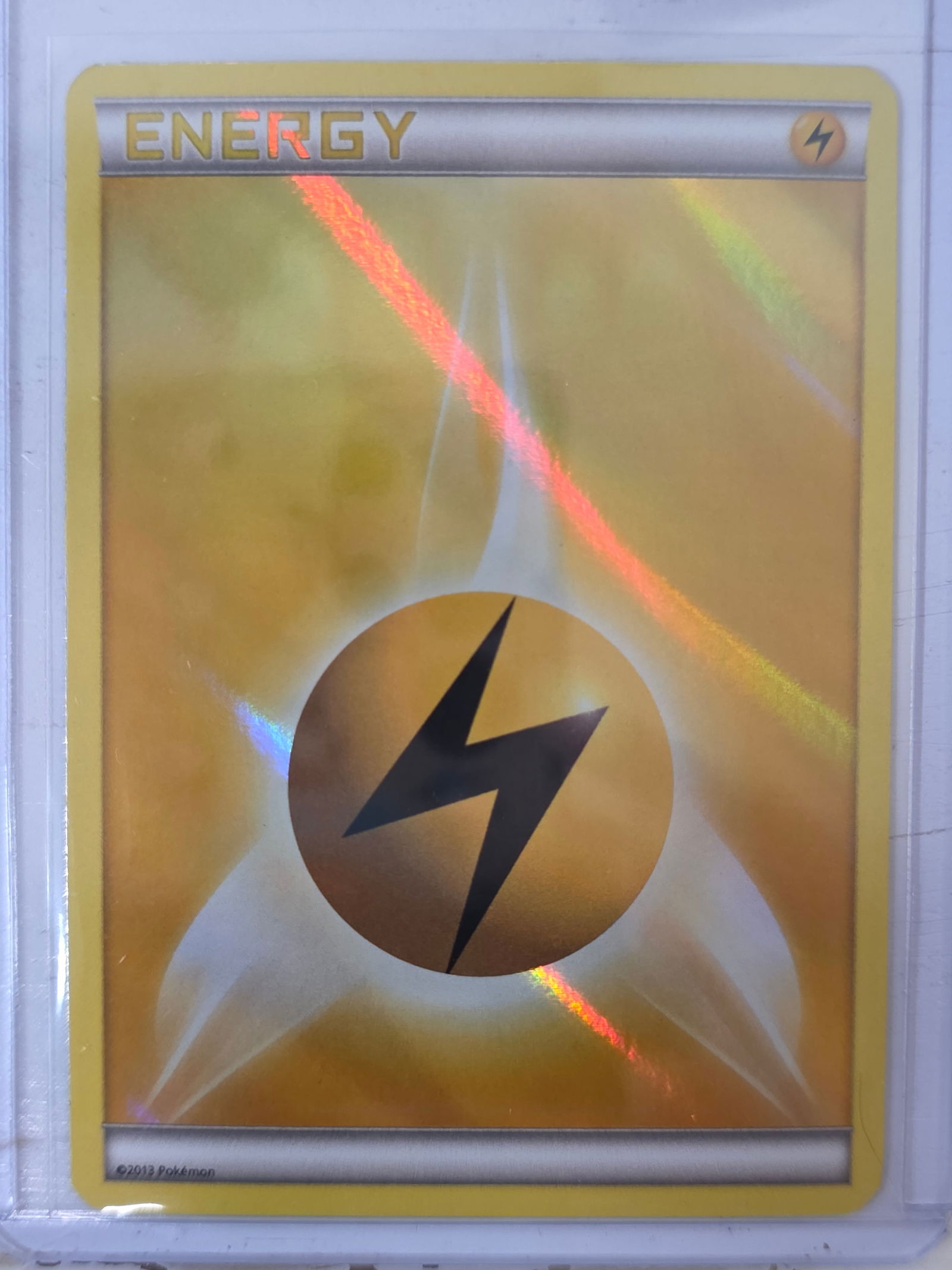 2013 Lightning Energy XY Base Set Reverse Holo Pokemon Card: 2013 Pokemon Lightning Energy reverse holo card from the XY Base Set expansion. Energy card featuring reverse holographic foil surface pattern. Card stored in penny sleeve and top loader.