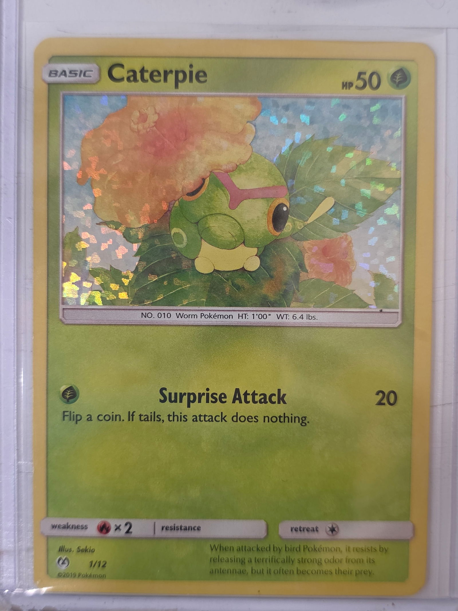2019 Caterpie Detective Pikachu 1/12 Holo Pokemon Card: 2019 Pokemon Caterpie holo card numbered 1/12 from the Detective Pikachu promotional mini set released alongside the Detective Pikachu film. Holographic confetti foil pattern across the illustration a
