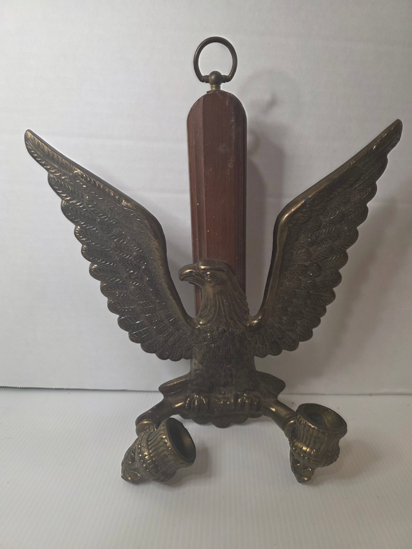 Vintage American Eagle Wall Sconce Brass Double Candle Holder USA: Vintage wall mounted candle sconce featuring a spread wing American eagle motif. The design is made of cast metal with a brass tone finish and supports two candle cups.The eagle is mounted on a wooden