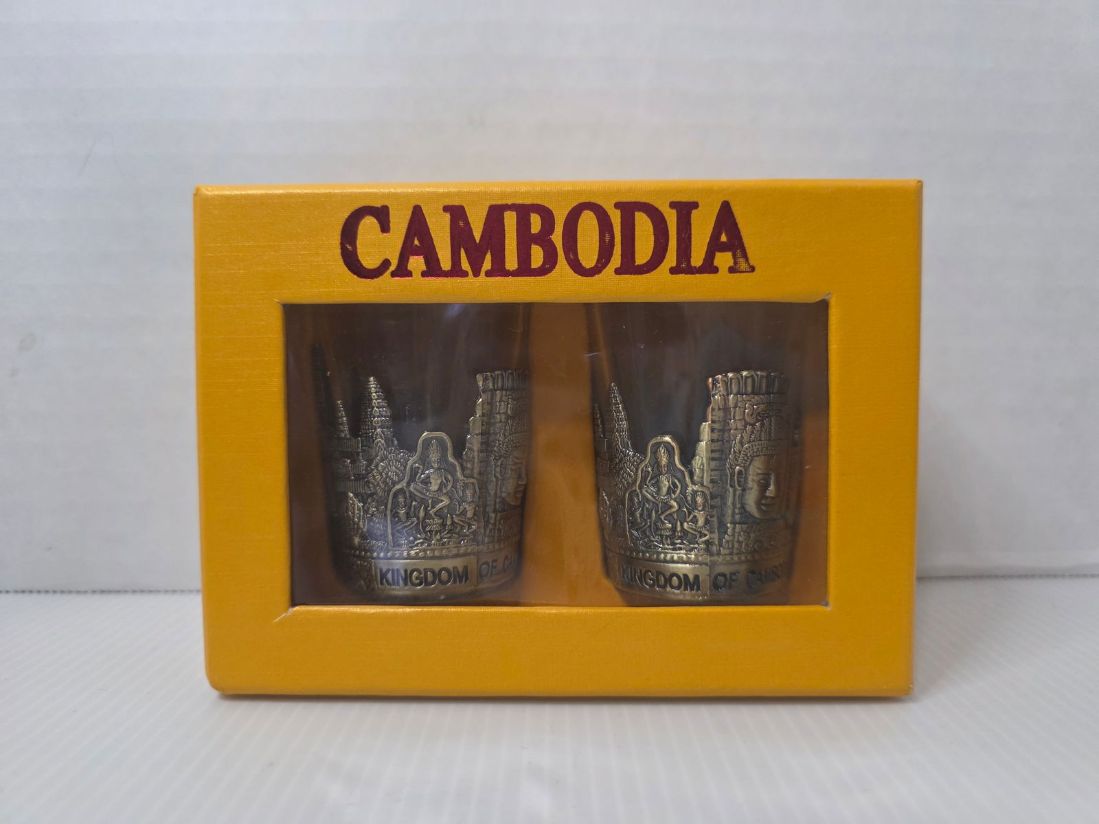 Cambodia Kingdom of Cambodia Souvenir Shot Glass Set Boxed: Cambodia Kingdom of Cambodia Souvenir Shot Glass Set Boxed Boxed souvenir Cambodia shot glass set featuring two clear glasses with raised metallic relief scenes representing Cambodian cultural and arc