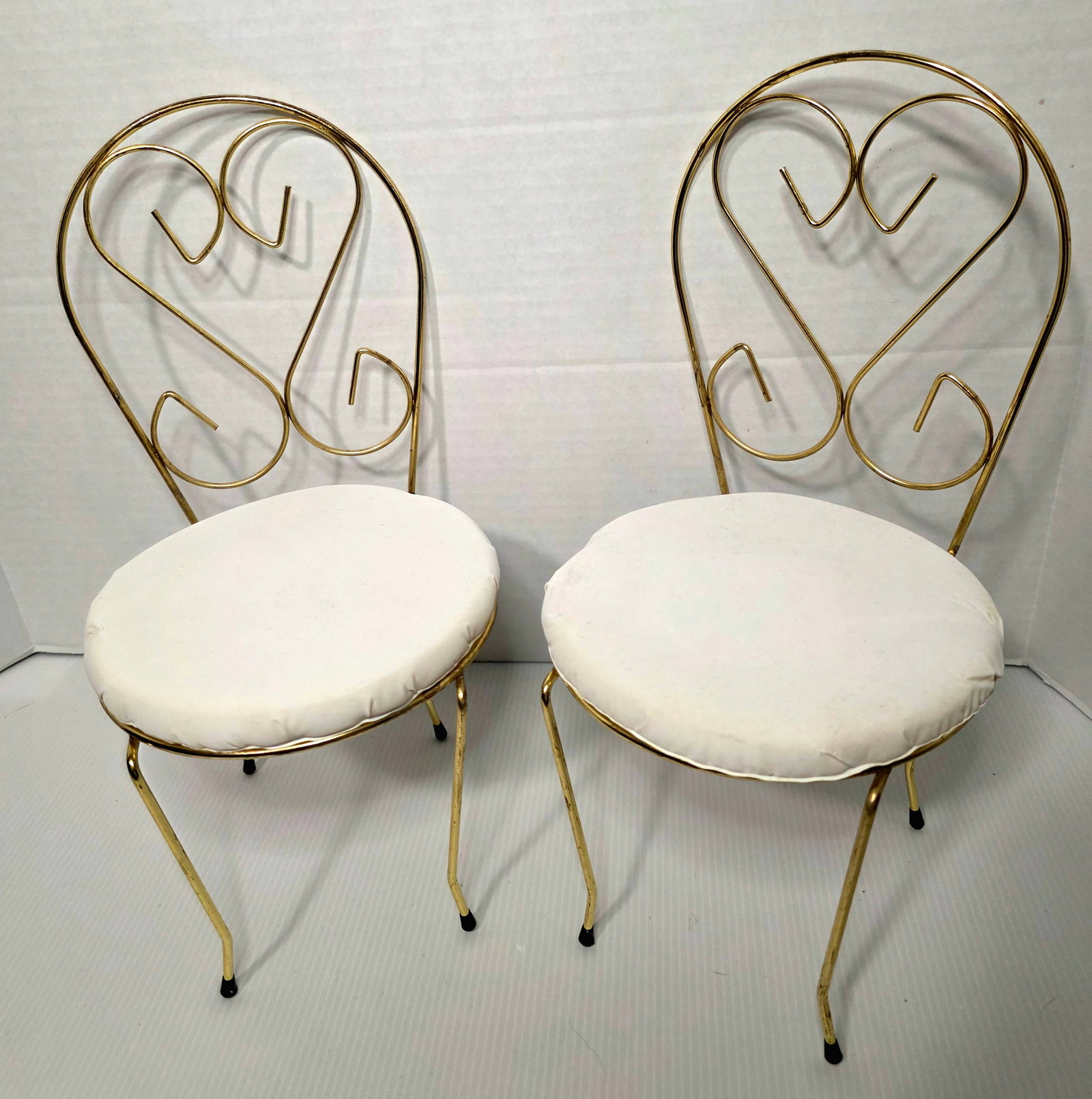 Pair Vintage Gold Tone Metal Vanity Chairs White Cushions Heart Back: Pair of vintage gold tone metal vanity or decorative chairs with heart scroll back design. Includes removable round white seat cushions. Lightweight metal construction with curved legs and rubber feet