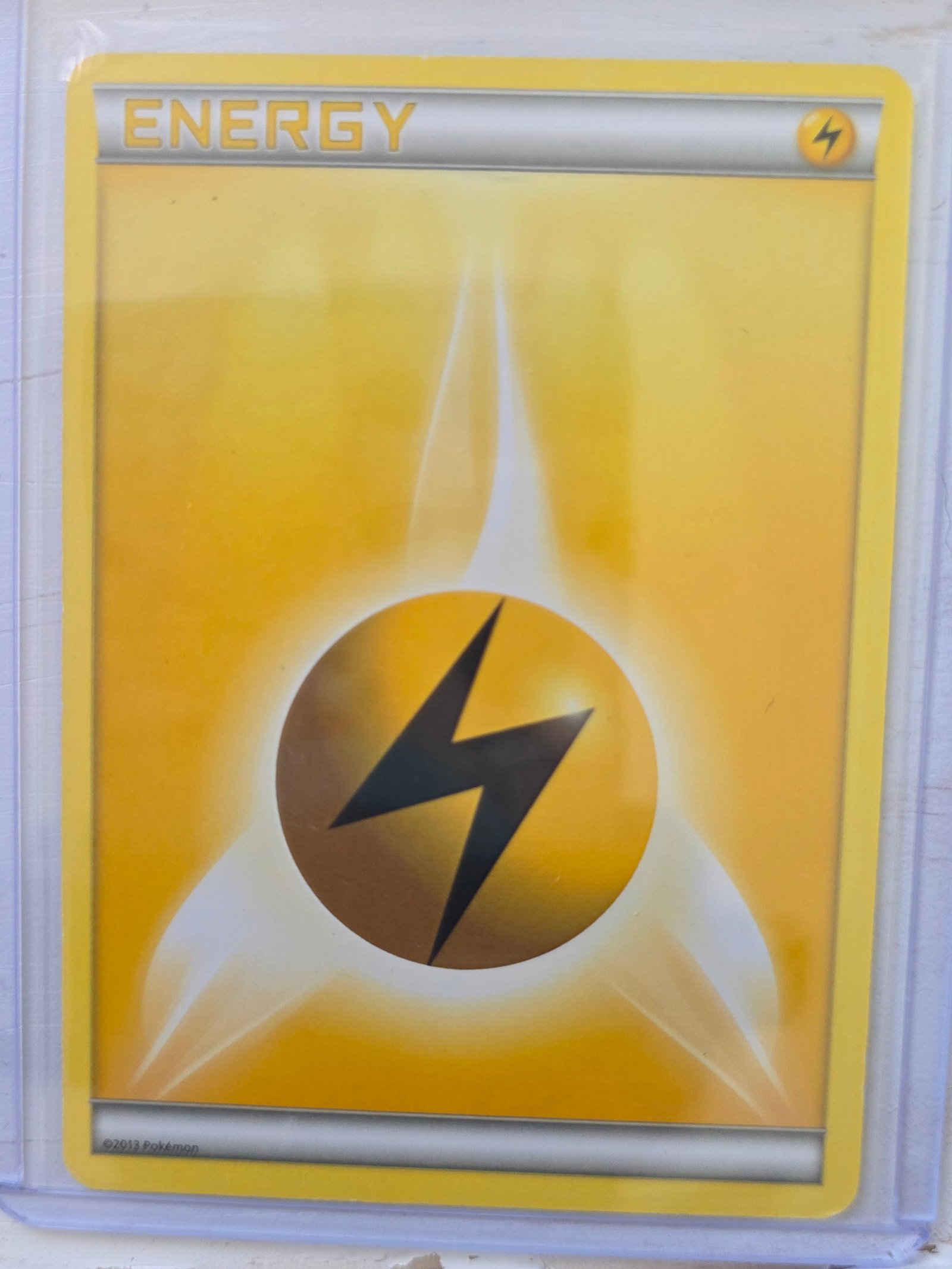 2013 Lightning Energy XY Basic: 2013 Lightning Energy Basic card. XY era yellow border design. Lightning bolt symbol centered. 2013 Pokemon. Non holo standard energy card. Preowned card stored in penny sleeve and top loader. Sold as