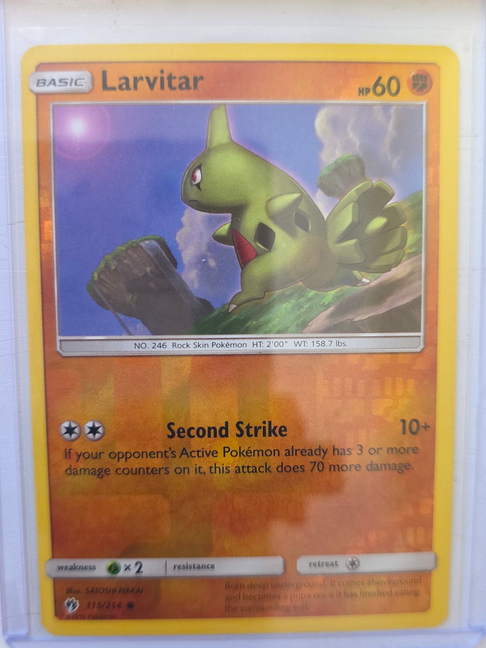 2018 Larvitar Lost Thunder 115/214 Reverse Holo Pokemon Card: 2018 Pokemon Larvitar reverse holo card numbered 115/214 from the Sun & Moon Lost Thunder expansion set. Illustrated by Satoshi Nakai. Reverse holographic foil pattern across the card surface. Card st