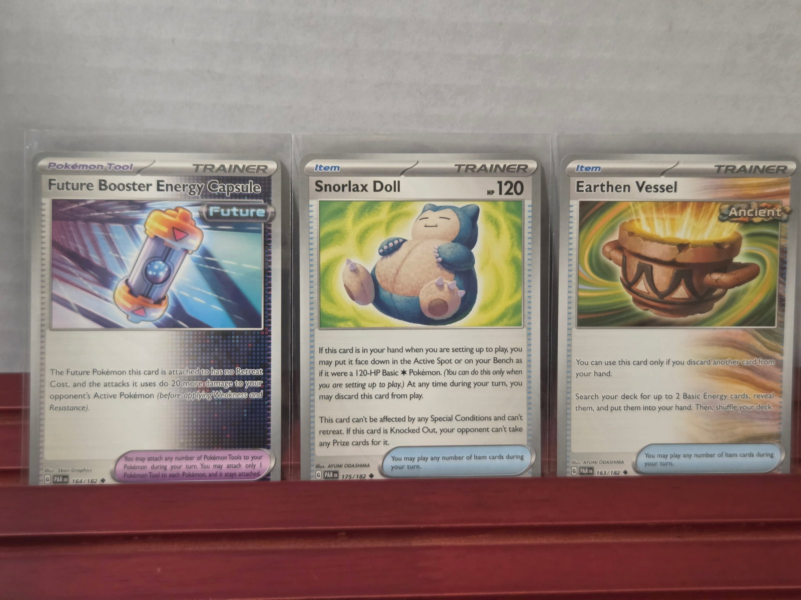 2023 Snorlax Doll Earthen Vessel Future Booster Trainer Lot: Trainer card lot featuring Snorlax Doll, Earthen Vessel, and Future Booster Energy Capsule. Includes both standard and reverse holo style cards with popular playable items. Solid addition for collecto
