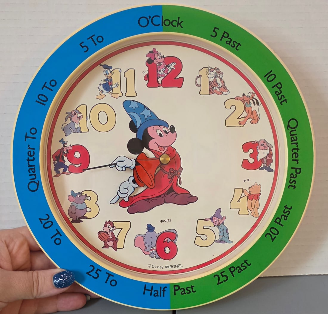 Disney Avronel Mickey Mouse Learning Time Wall Clock Quartz: Disney Avronel quartz wall clock featuring Sorcerer Mickey at center with classic Disney characters at each hour. Outer ring displays learning time markers such as “quarter past,” “half past