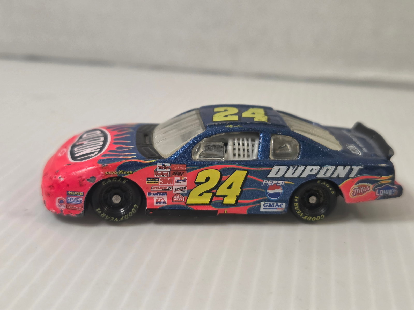 Jeff Gordon #24 DuPont Chevy Monte Carlo NASCAR Diecast 2002: This diecast model represents the #24 DuPont Chevrolet Monte Carlo driven by Jeff Gordon in NASCAR competition. The car features the iconic blue and red DuPont flame paint scheme along with sponsor lo